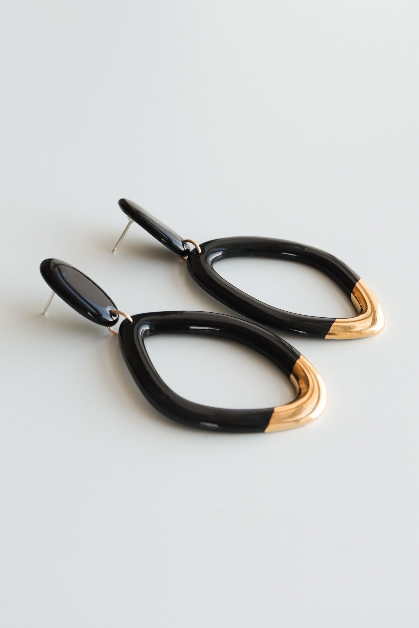 The Flow Earrings by Rozenthal Jewelry are modern, teardrop-shaped, hypoallergenic designer earrings with black and gold accents, handmade in Latvia and shown on a light, neutral background.