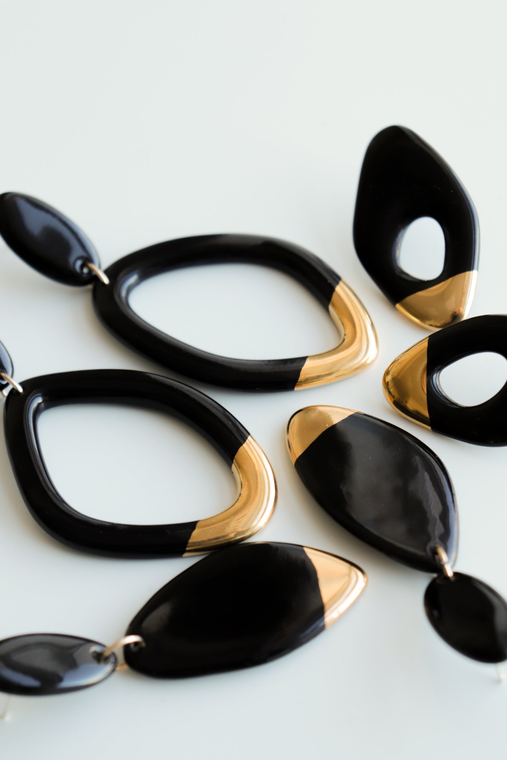 A close-up of Rozenthal Jewelry’s Flow Earrings, modern handmade pieces in black and gold with abstract oval and teardrop shapes, displayed on a white surface.