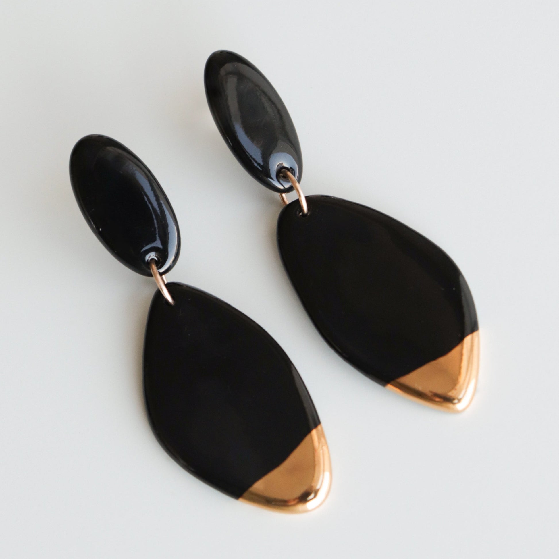 Flow Earrings by Rozenthal Jewelry: modern handmade porcelain earrings with black oval studs, matching black pendants, and gold-toned tips—perfect statement pieces for any occasion. Displayed on a light surface.
