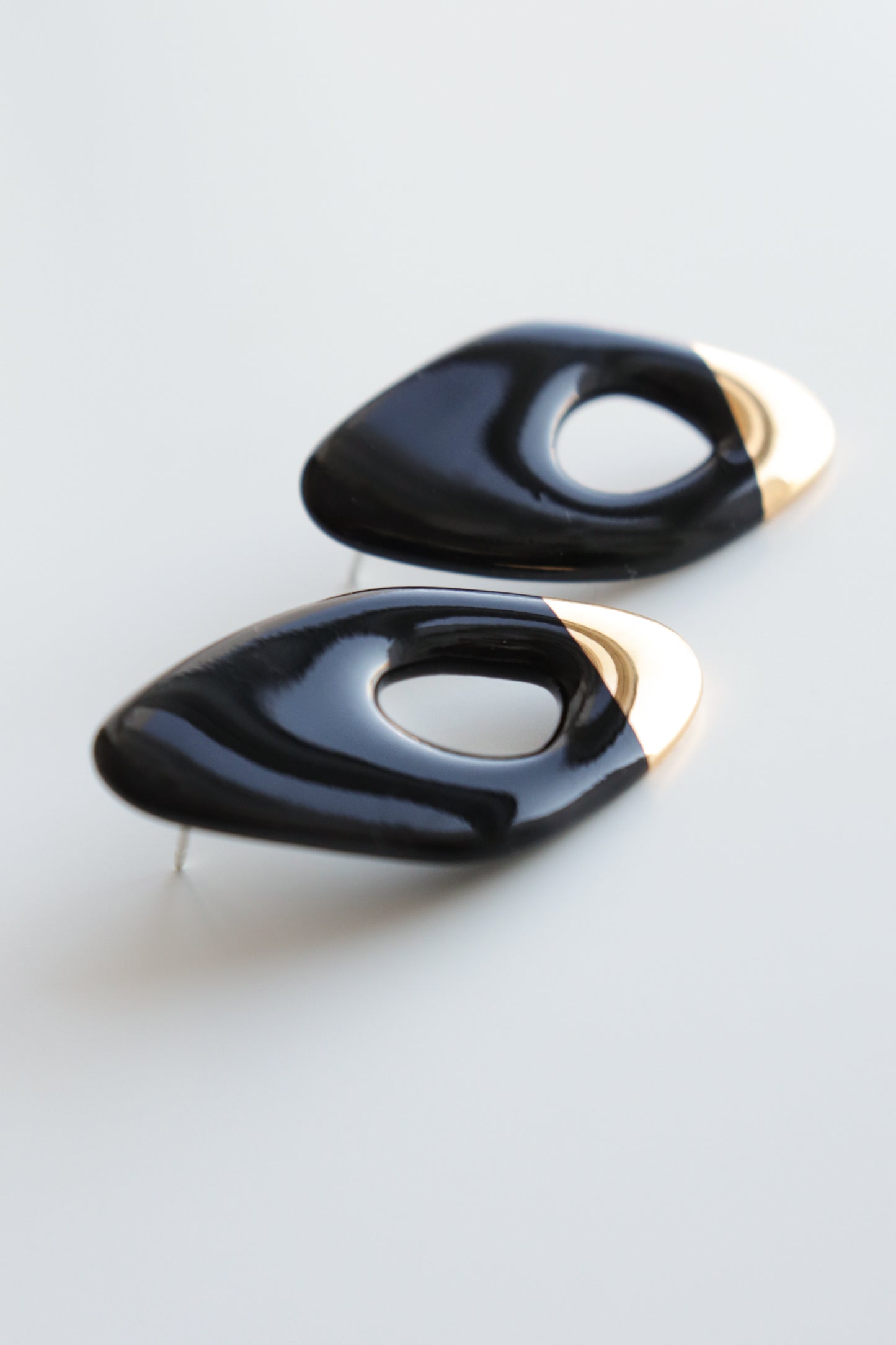 Flow Earrings by Rozenthal Jewelry: modern, asymmetrical handmade black earrings with glossy finish and metallic gold accents, each featuring an off-center oval cutout, displayed on a white surface.