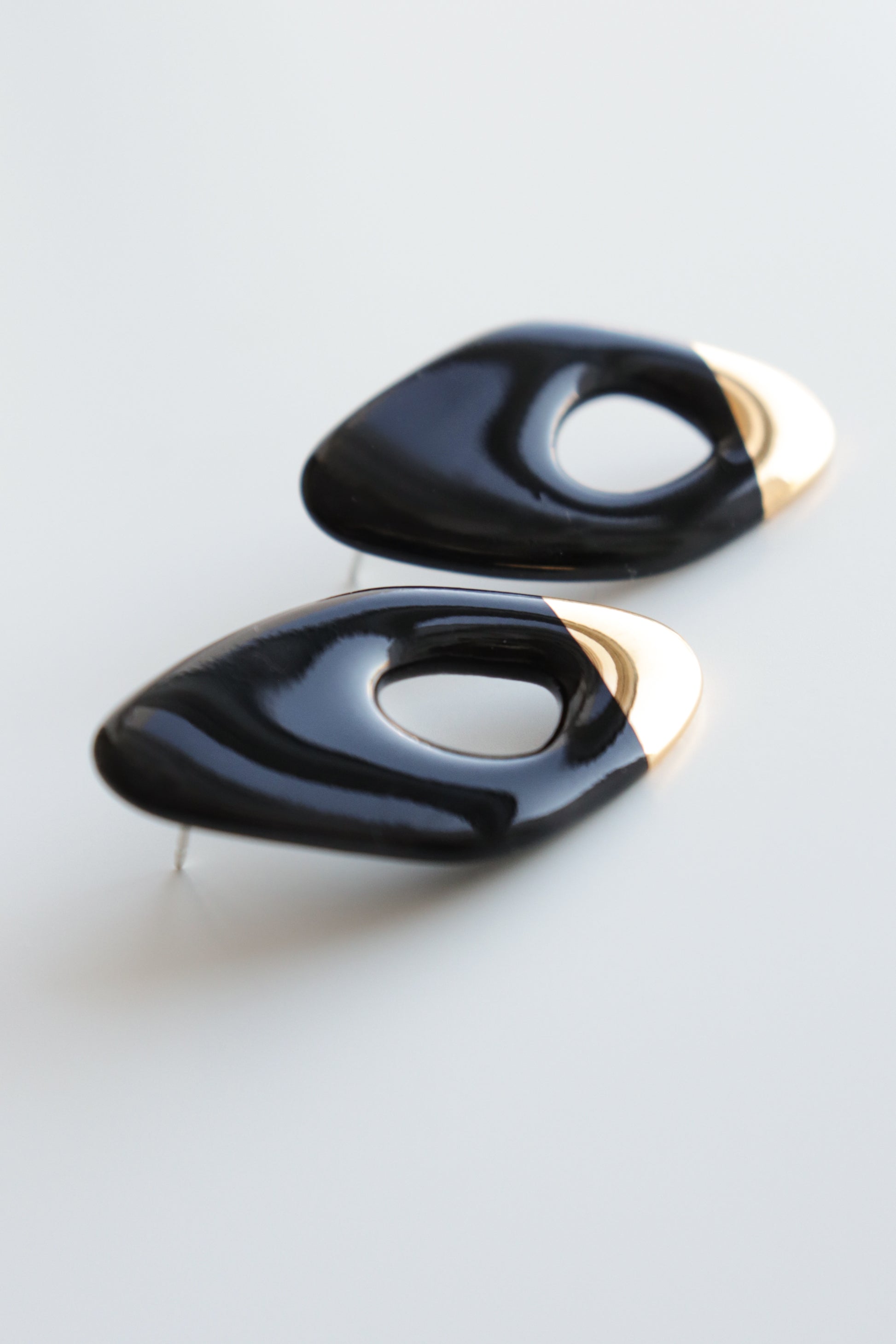 Flow Earrings by Rozenthal Jewelry: modern, asymmetrical handmade black earrings with glossy finish and metallic gold accents, each featuring an off-center oval cutout, displayed on a white surface.