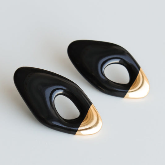 The Flow Earrings by Rozenthal Jewelry are handmade, black, abstract-shaped earrings with open centers and gold tips, shown on a plain white background.