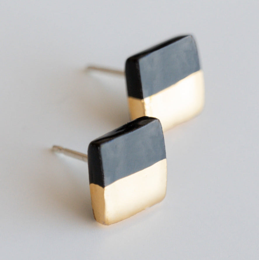 Rozenthal Jewelry’s Edgy Studs / XS are square, color-block earrings with a black top half and gold bottom half, displayed on a white background—ideal for minimalist jewelry lovers.