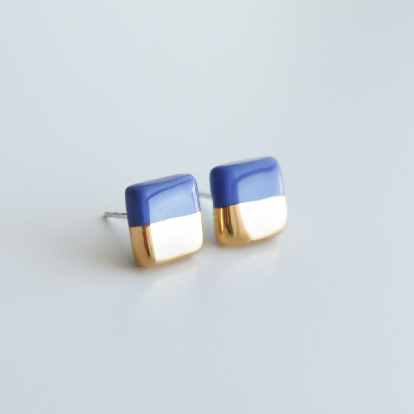 Edgy Studs / XS by Rozenthal Jewelry feature a glossy blue top and shiny gold bottom in a square design. These minimalist earrings offer elegant style, shown against a plain white background.