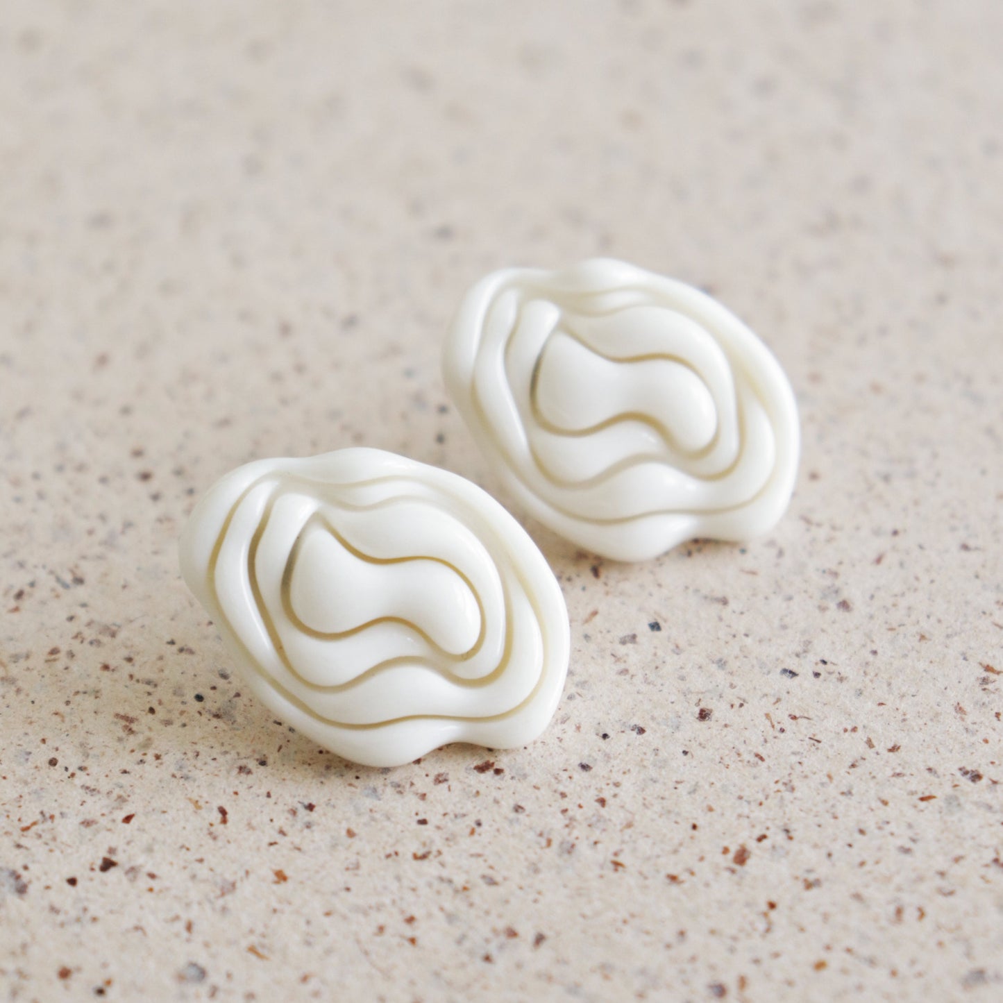 Pair of white textured earrings on a beige surface