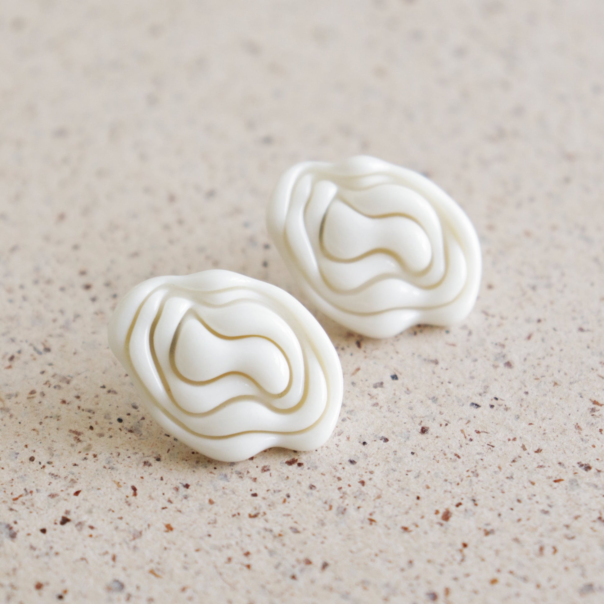 Pair of white textured earrings on a beige surface