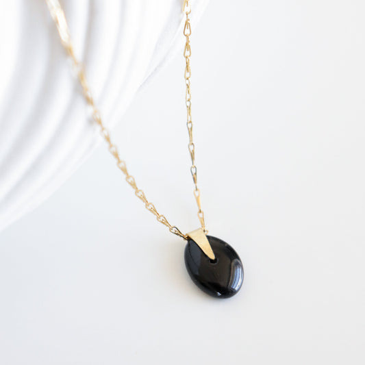 Gold necklace with a black pendant on a white background