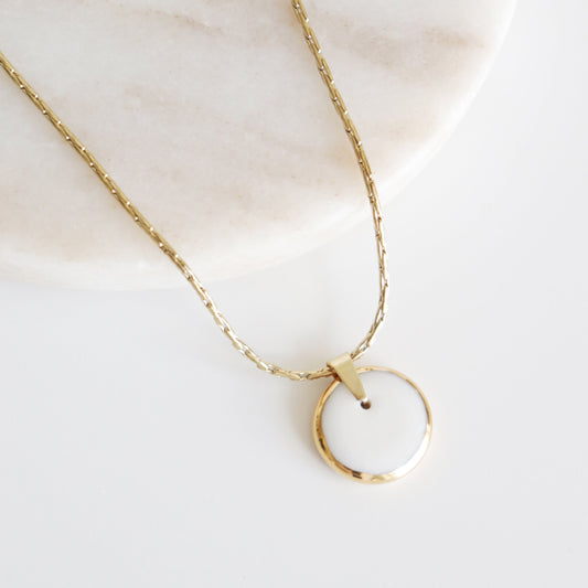 Gold necklace with a circular pendant on a light background