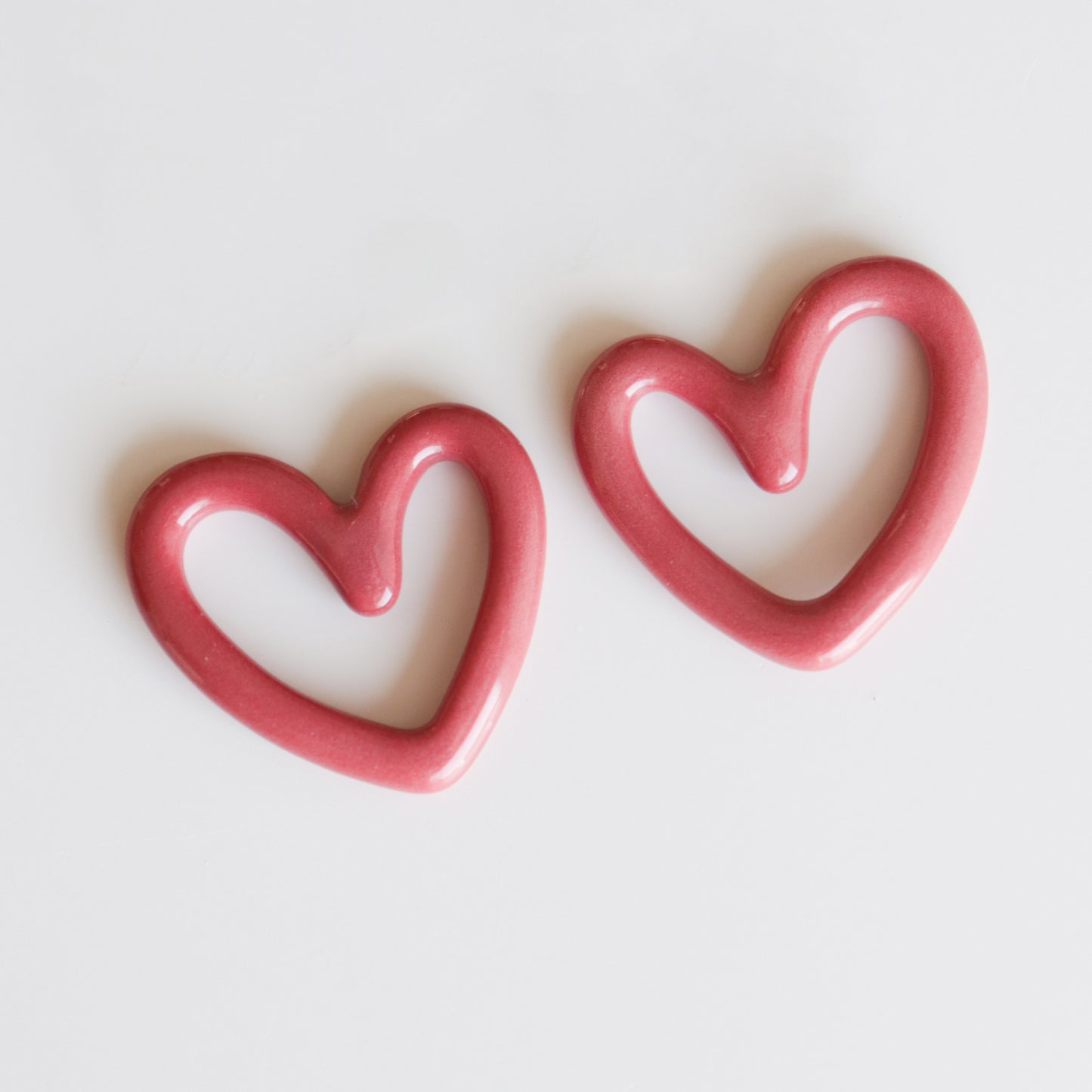Two pink, heart-shaped Rozenthal Jewelry Heart Earrings with open centers are displayed on a white background, slightly tilted—lightweight, waterproof, and hypoallergenic designer earrings.