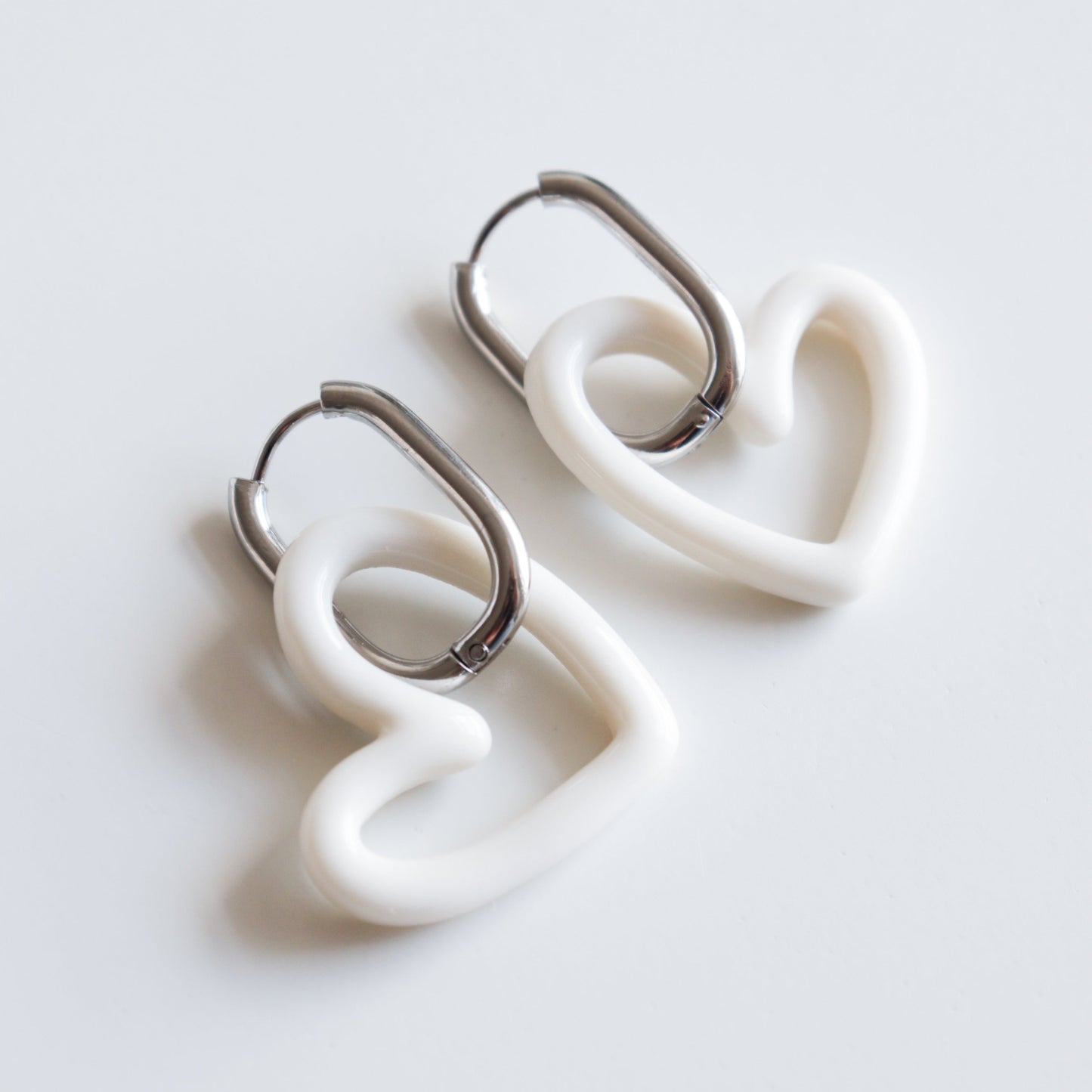 Rozenthal Jewelry Heart Earrings feature lightweight, waterproof, white heart-shaped charms on silver hoops, shown against a plain white background.
