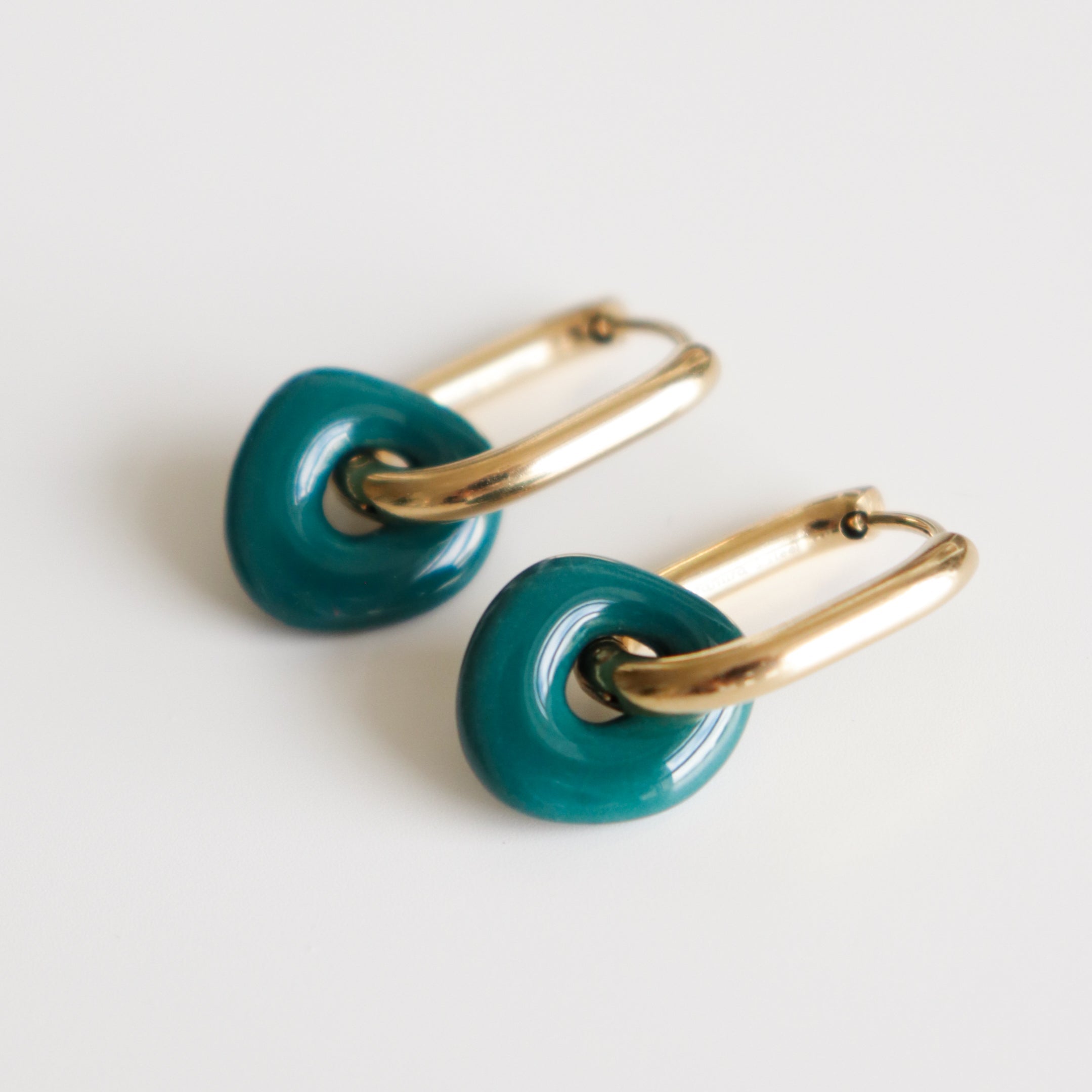 Pair of earrings with dark green circular charms and gold loops on a light gray background