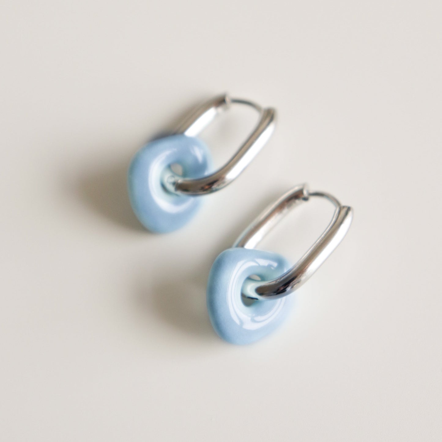 Pair of light blue hoop earrings with silver hoops on a light gray background
