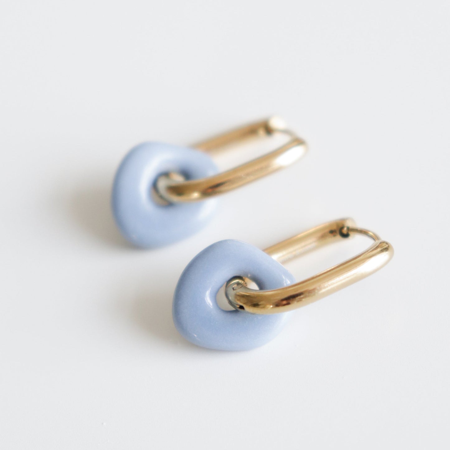 Pair of earrings with gold loops and periwinkle ceramic parts on a white background