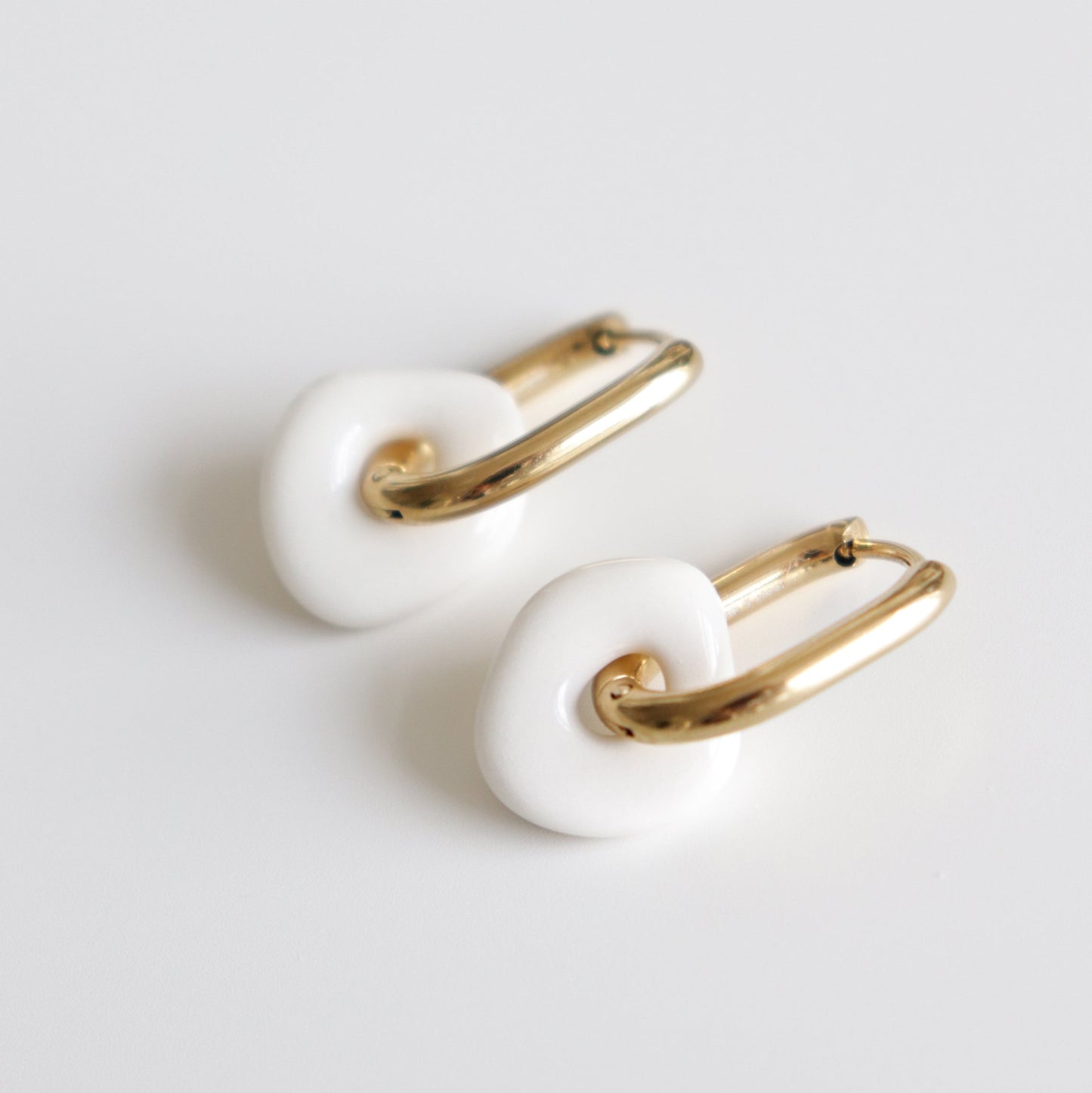 Pair of gold and white hoop earrings on a light gray background