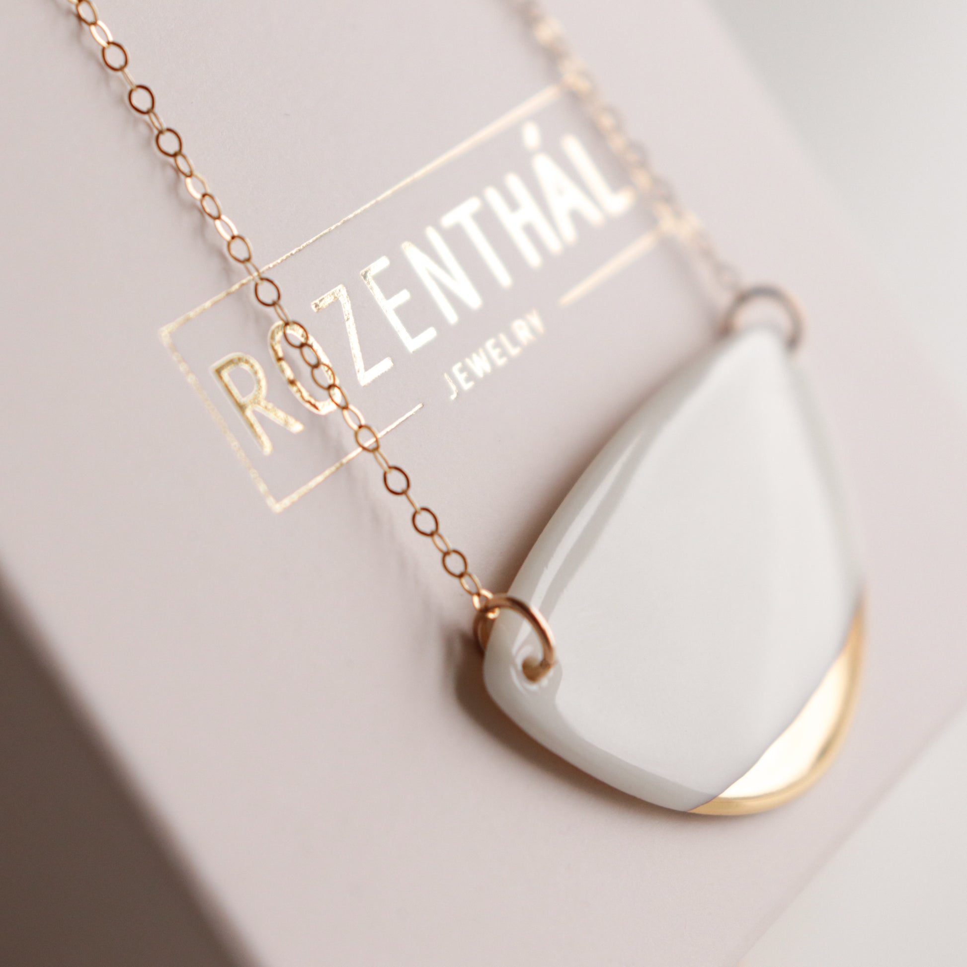 Close-up of a white and gold Leaf Necklace pendant on a delicate chain, displayed on a card with Rozenthal Jewelry embossed in gold—a stunning piece of minimalist jewelry.