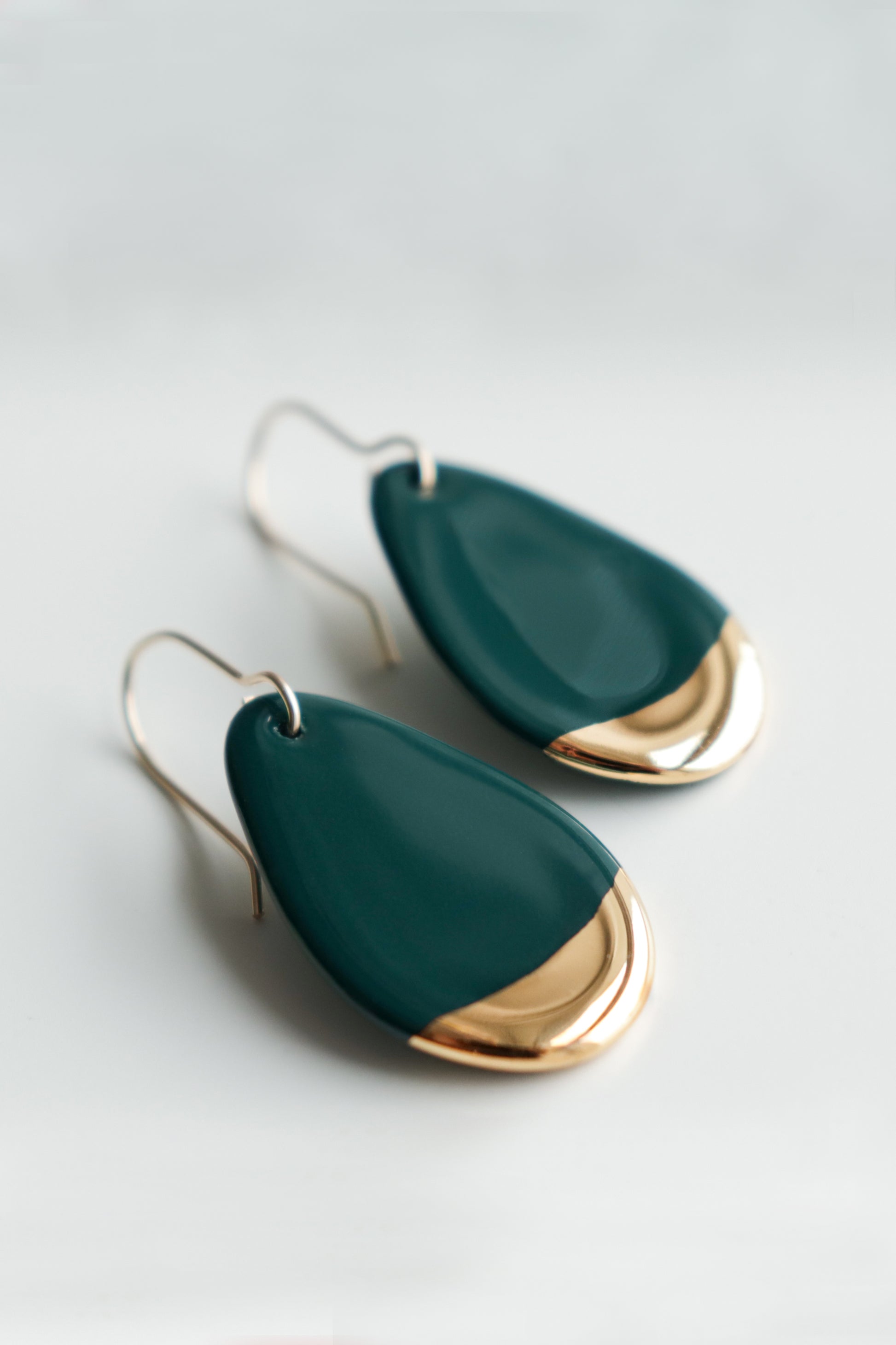 The Drop Earrings / S by Rozenthal Jewelry are teardrop-shaped with dark green bodies and shiny gold tips, featuring simple metal hooks. These handmade earrings are displayed against a white background.