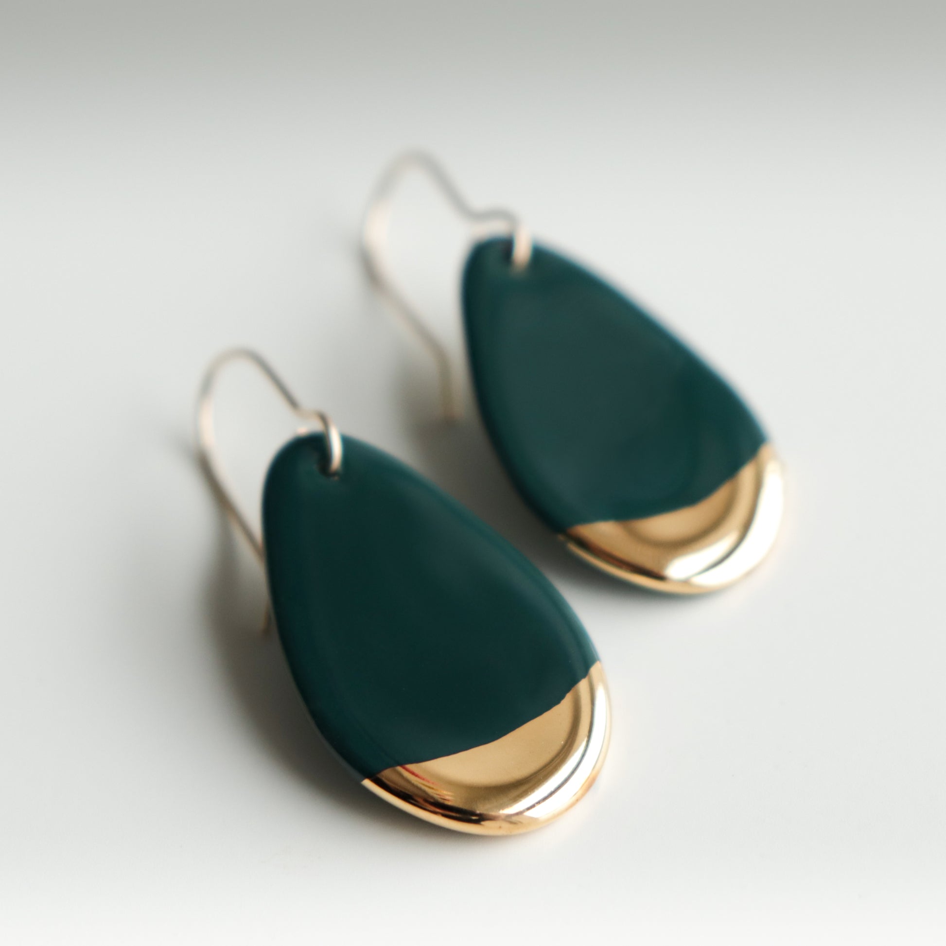 Drop Earrings / S by Rozenthal Jewelry: handmade porcelain teardrop earrings featuring dark green bodies and shiny gold-colored tips, displayed on a light neutral background.