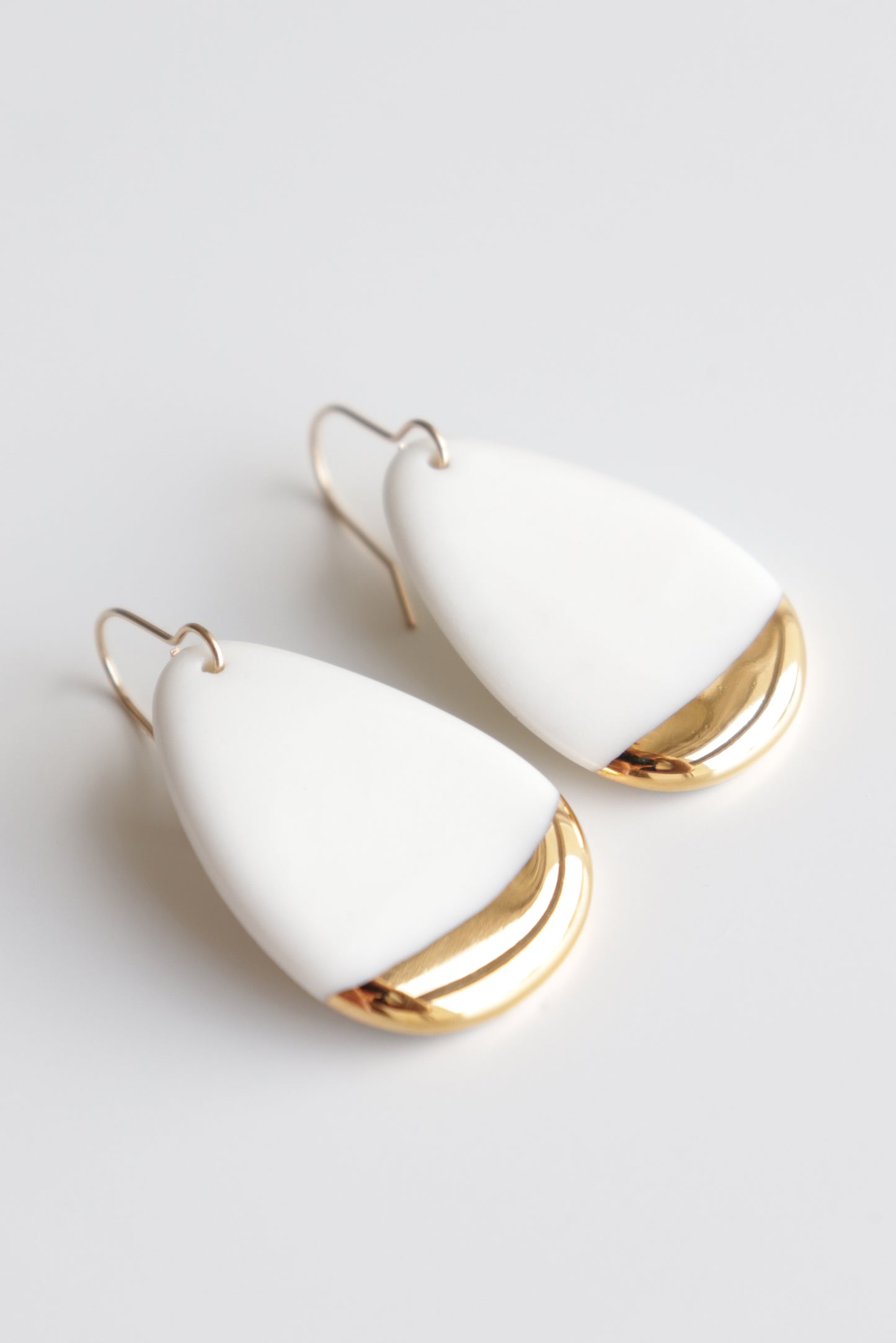 The Rozenthal Jewelry Drop Earrings / M are handmade teardrop-shaped porcelain statement earrings, featuring a smooth white upper part and a shiny gold lower edge, shown on a white background.