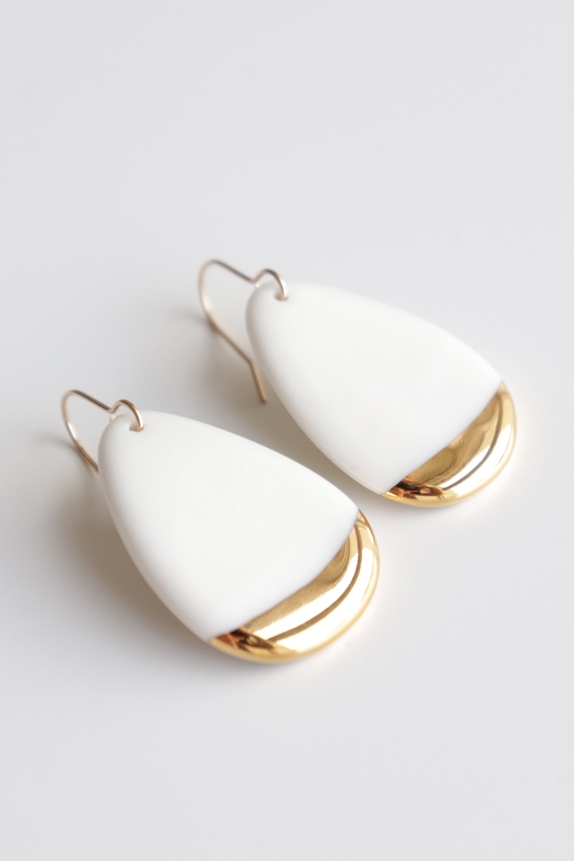 The Rozenthal Jewelry Drop Earrings / M are handmade teardrop-shaped porcelain statement earrings, featuring a smooth white upper part and a shiny gold lower edge, shown on a white background.