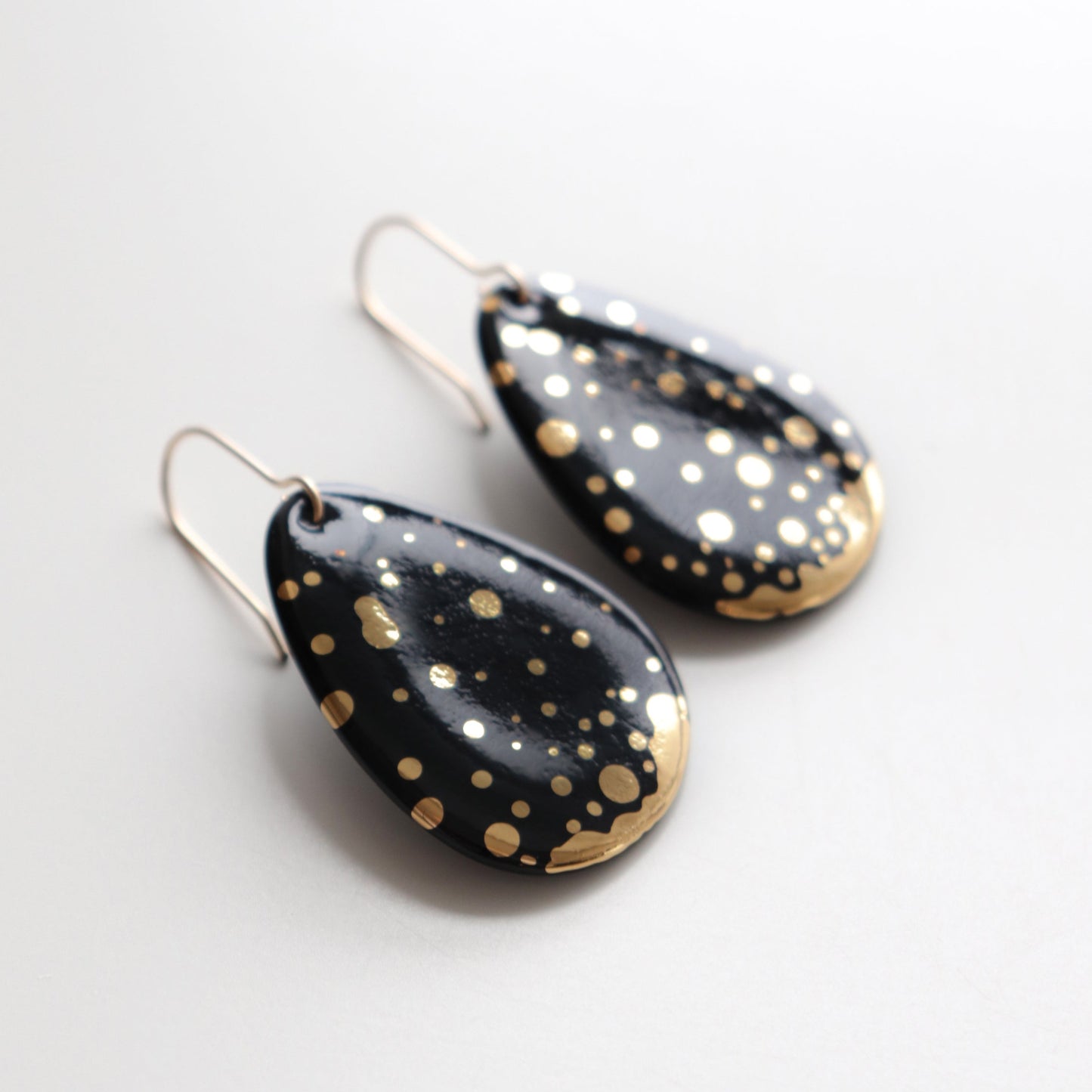 Rozenthal Jewelry’s Drop Earrings / M feature black porcelain teardrops with gold polka dots and metallic hooks, displayed on a light surface.