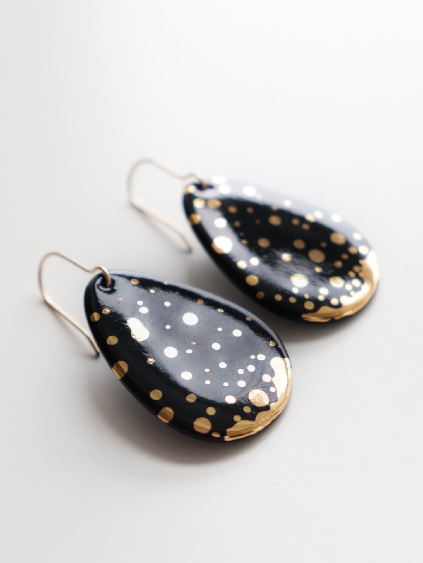 A pair of Drop Earrings / M by Rozenthal Jewelry, teardrop-shaped and hypoallergenic, featuring a glossy black finish with scattered gold accents, displayed on a white background.