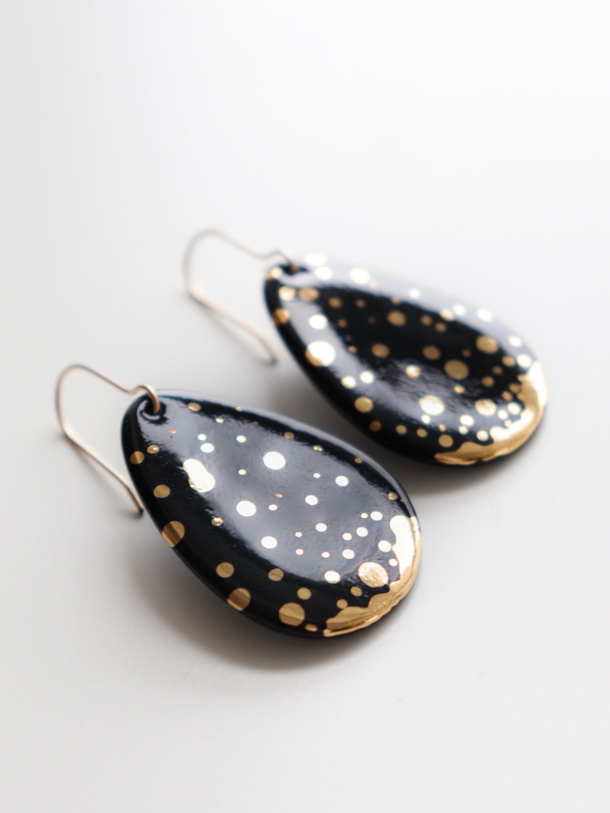 A pair of Drop Earrings / M by Rozenthal Jewelry, teardrop-shaped and hypoallergenic, featuring a glossy black finish with scattered gold accents, displayed on a white background.