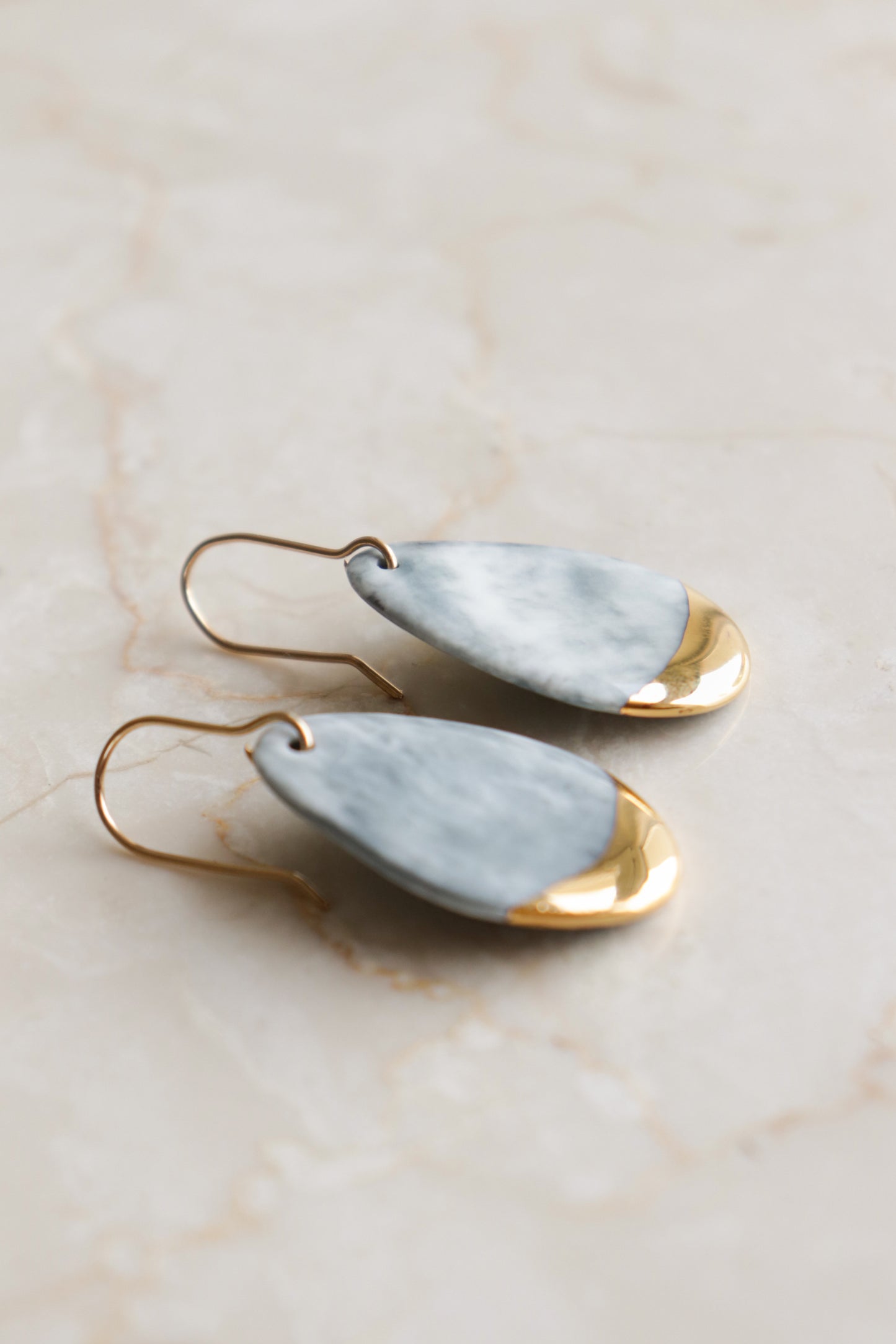 Rozenthal Jewelrys Drop Earrings / S: teardrop-shaped, hypoallergenic designer earrings with marbled light gray tops and shiny gold bottoms, shown on a light beige marble surface.