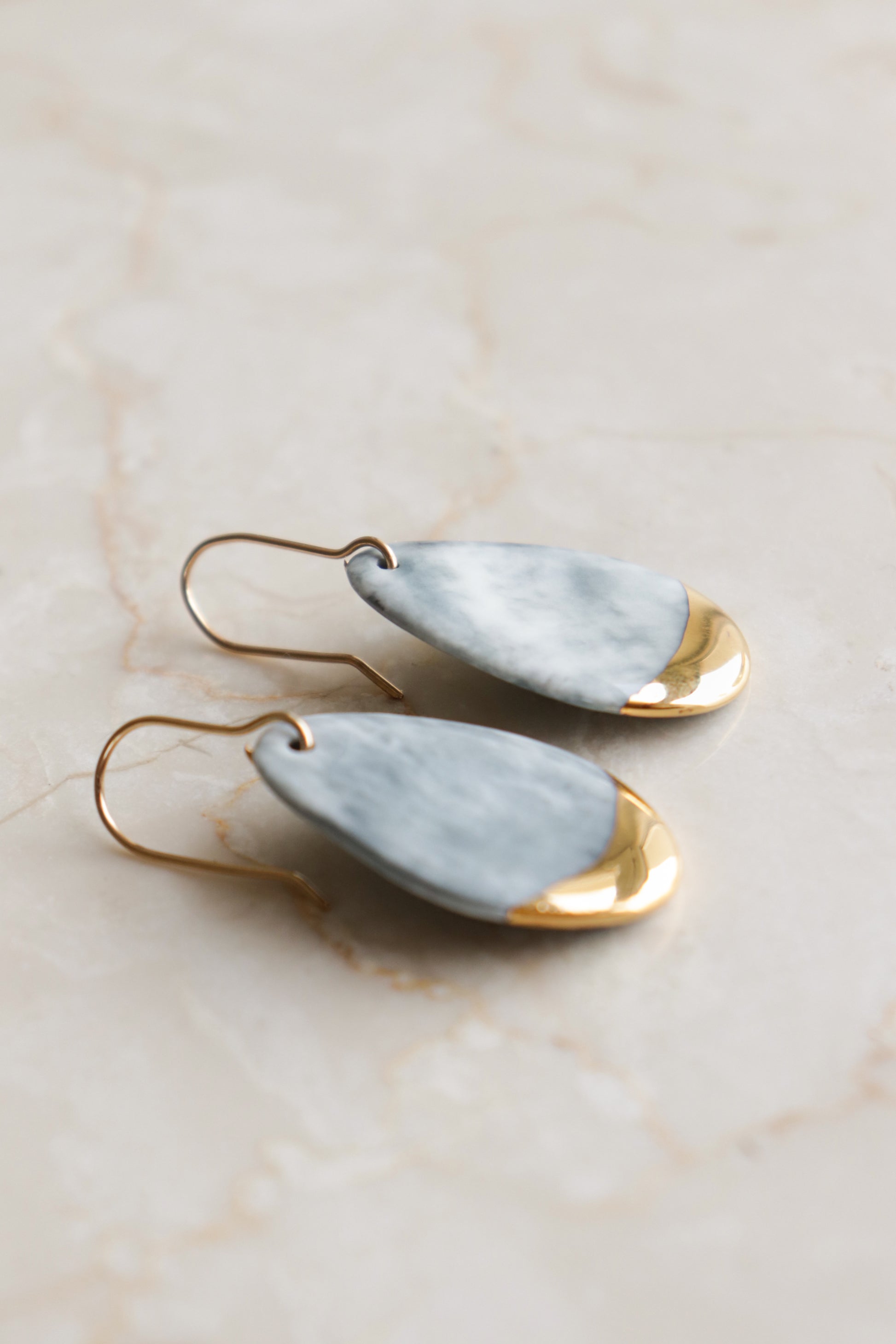 Rozenthal Jewelrys Drop Earrings / S: teardrop-shaped, hypoallergenic designer earrings with marbled light gray tops and shiny gold bottoms, shown on a light beige marble surface.