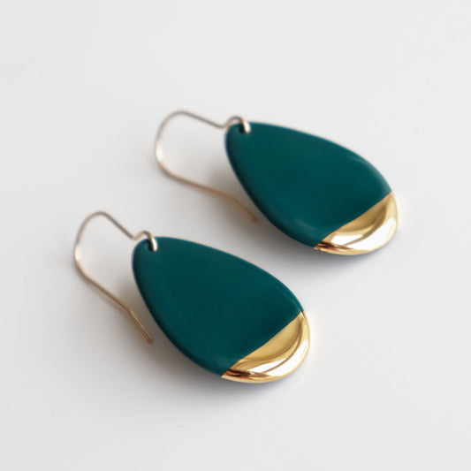 The Drop Earrings / S by Rozenthal Jewelry are teardrop-shaped porcelain pieces with teal bodies and gold-toned tips, featuring simple hooks—an elegant minimalist accessory shown on a white background.