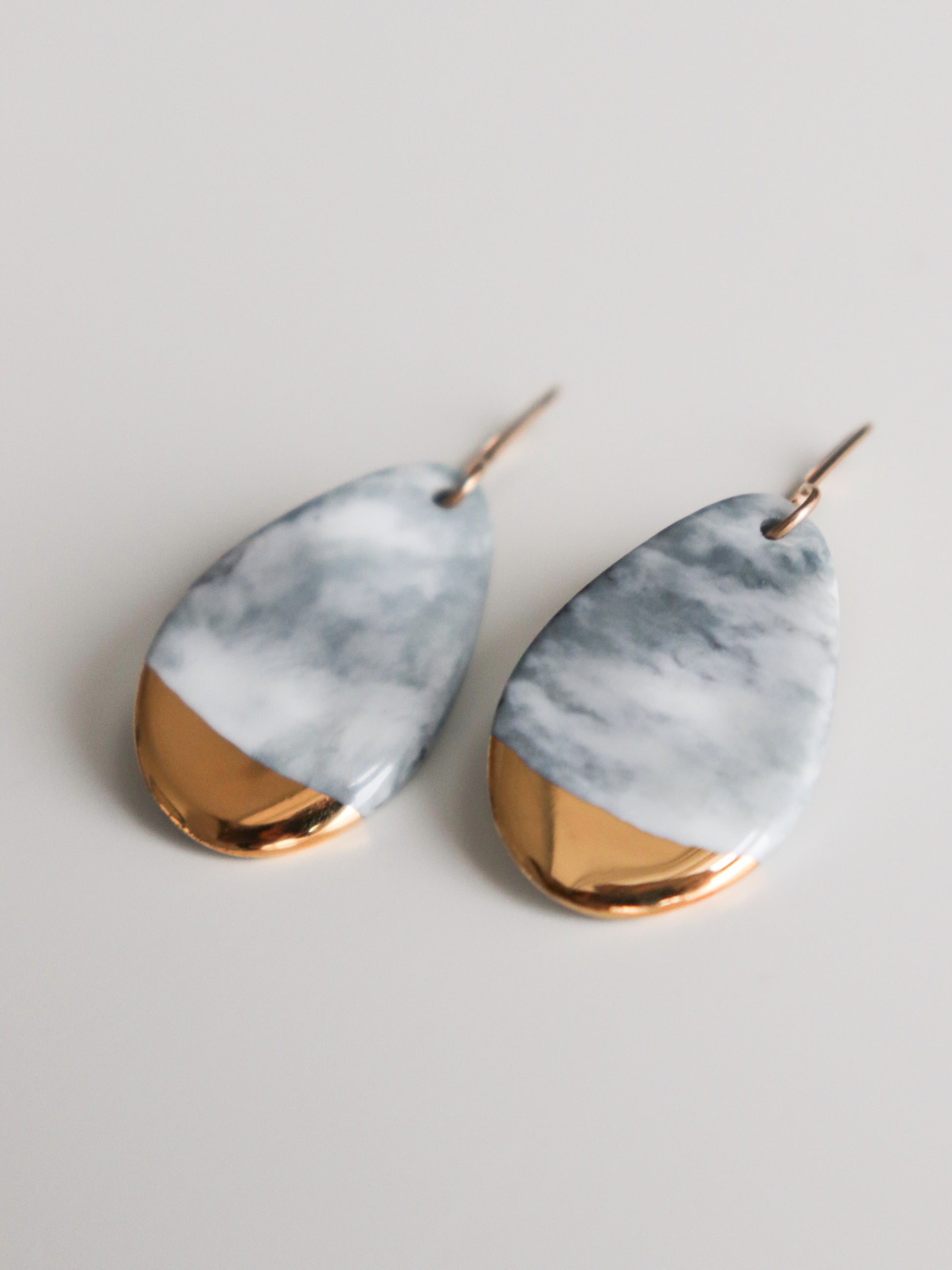 The Drop Earrings / S by Rozenthal Jewelry are teardrop-shaped, handmade with a marbled gray and white pattern, each accented with gold at the bottom. Displayed on a simple light background, these earrings are sustainable and crafted with care.