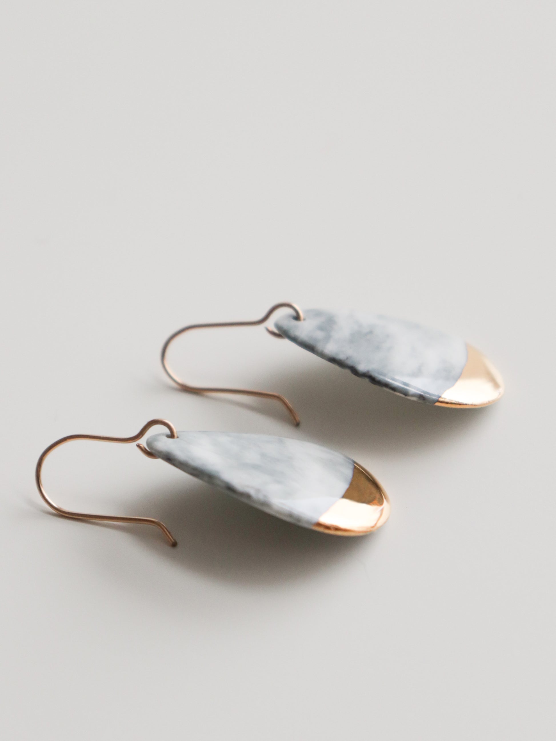 Drop Earrings / S by Rozenthal Jewelry—handmade teardrop porcelain statement earrings with marbled white and gray tops, shiny gold tips, and gold hooks. Made in Latvia, shown against a plain white background.