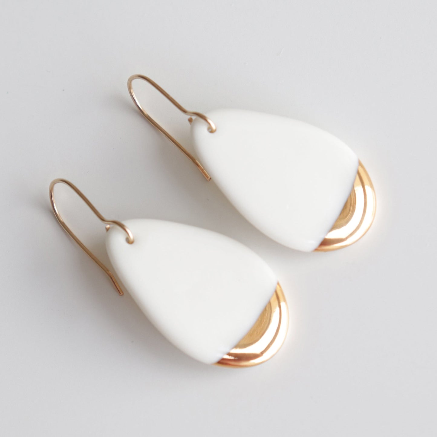 Rozenthal Jewelry’s Drop Earrings / S feature teardrop-shaped white pendants and gold hooks with shiny gold accents. These minimalist earrings are displayed against a simple light background.