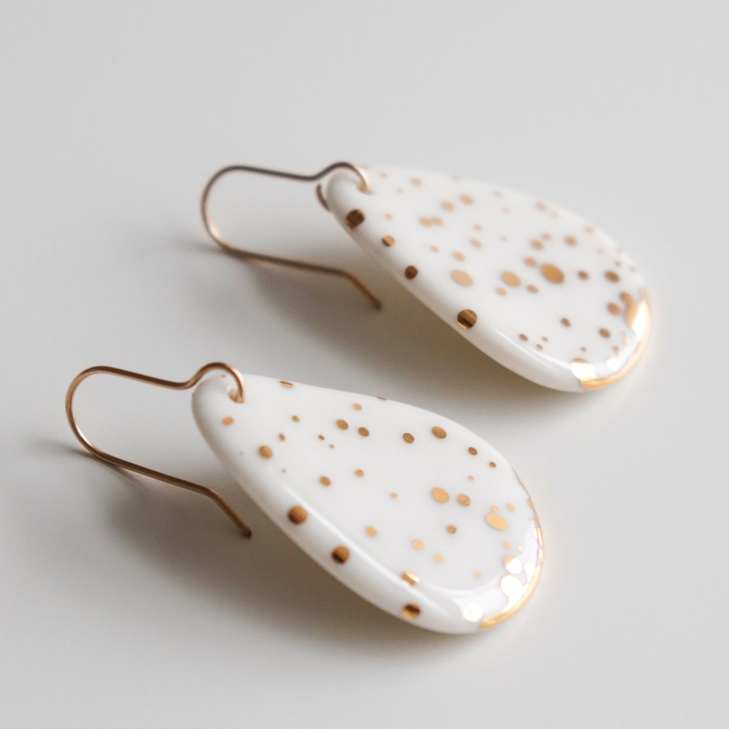 Drop Earrings / M by Rozenthal Jewelry: elegant white porcelain teardrop statement earrings with gold speckles and gold hooks, shown on a plain white background.