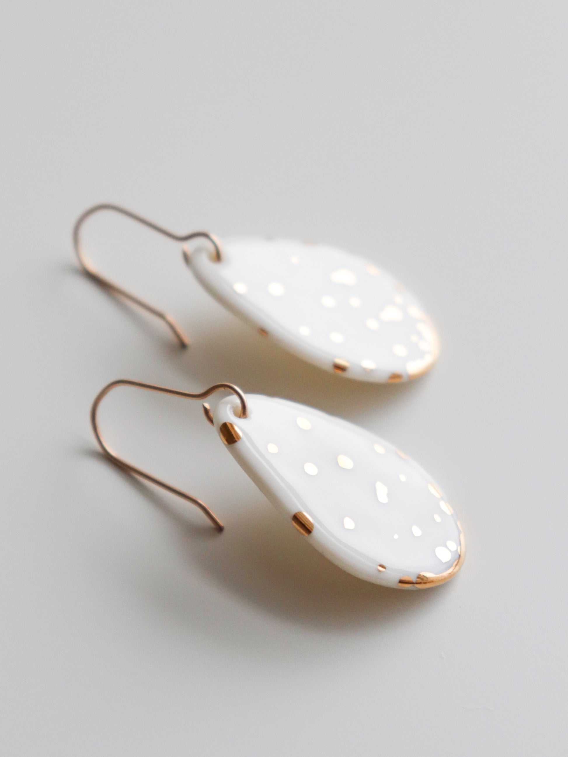 Handmade in Latvia, the Rozenthal Jewelry Drop Earrings / S are white porcelain teardrop statement earrings with gold speckles and gold hooks, shown on a light gray background.