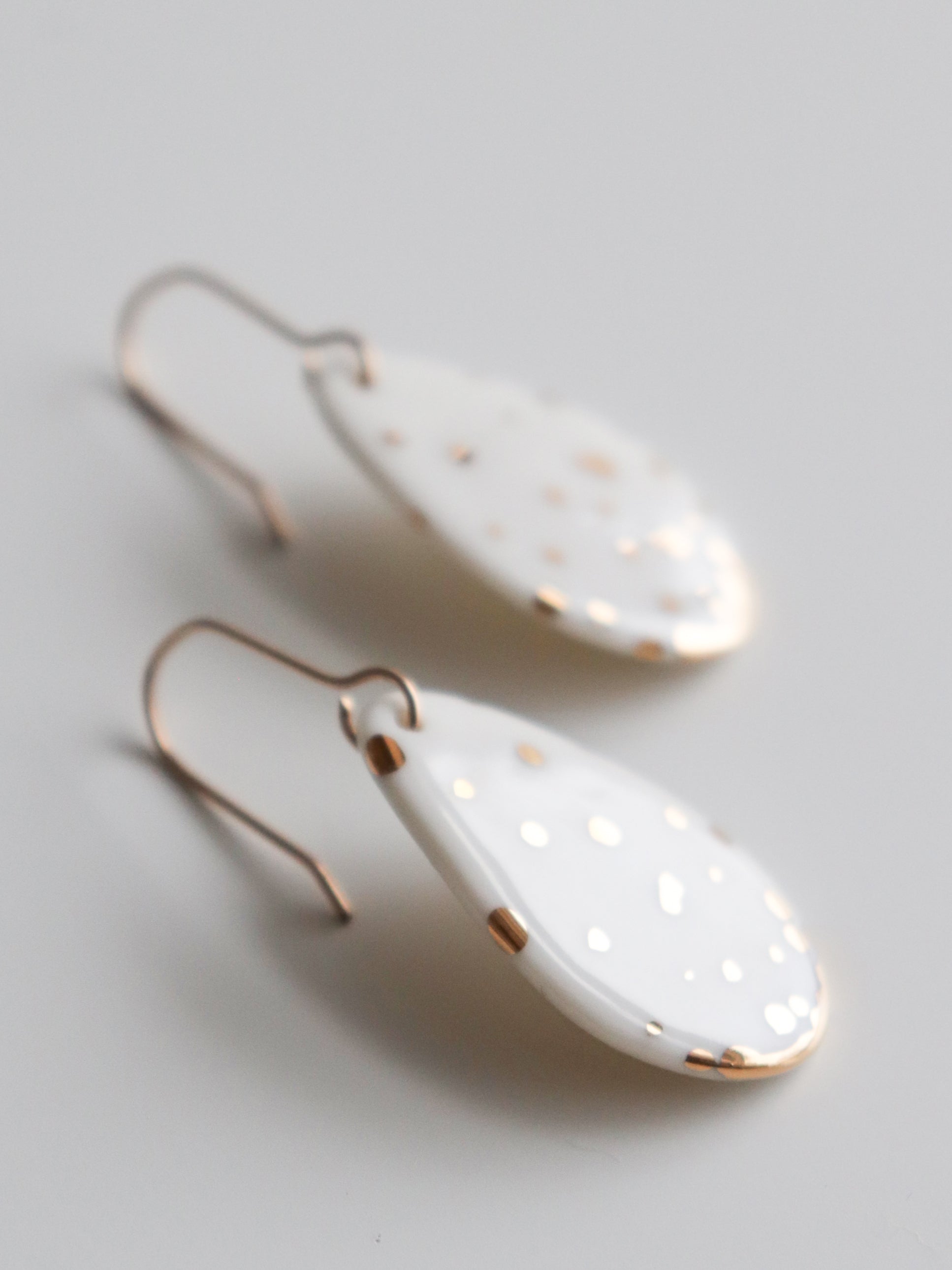 Rozenthal Jewelrys Drop Earrings / S are teardrop-shaped, white, hypoallergenic designer earrings with small gold dots and trim. Lightweight and perfect for sensitive ears, they feature simple gold hooks and are shown on a white background.
