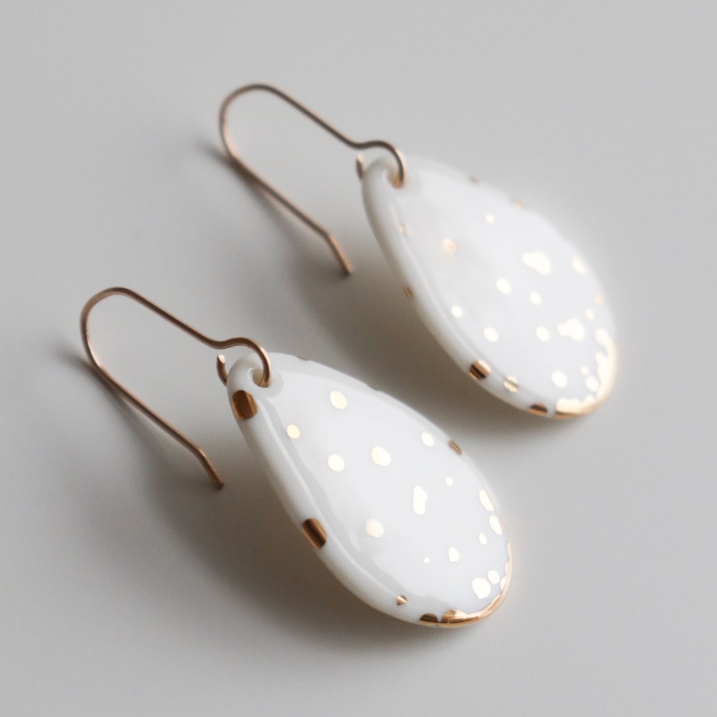 Drop Earrings / S by Rozenthal Jewelry: handmade teardrop-shaped white porcelain earrings with gold speckles and hooks, lightweight and waterproof. Made in Latvia, shown on a light grey background.