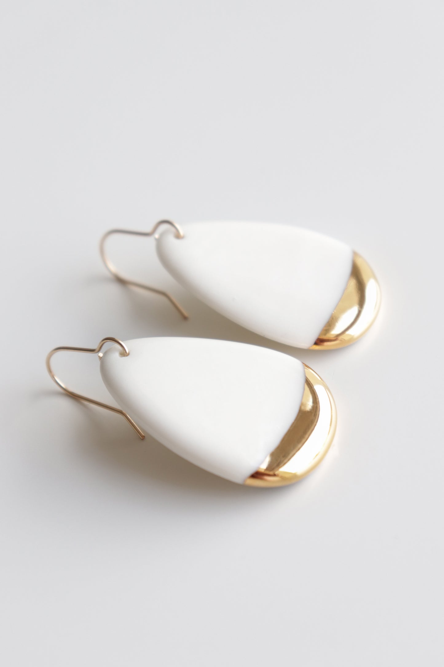 Rozenthal Jewelrys Drop Earrings / M feature teardrop-shaped, handmade white earrings with a gold metallic accent. Lightweight and waterproof, they’re perfect for everyday elegance and rest beautifully on a plain light background.