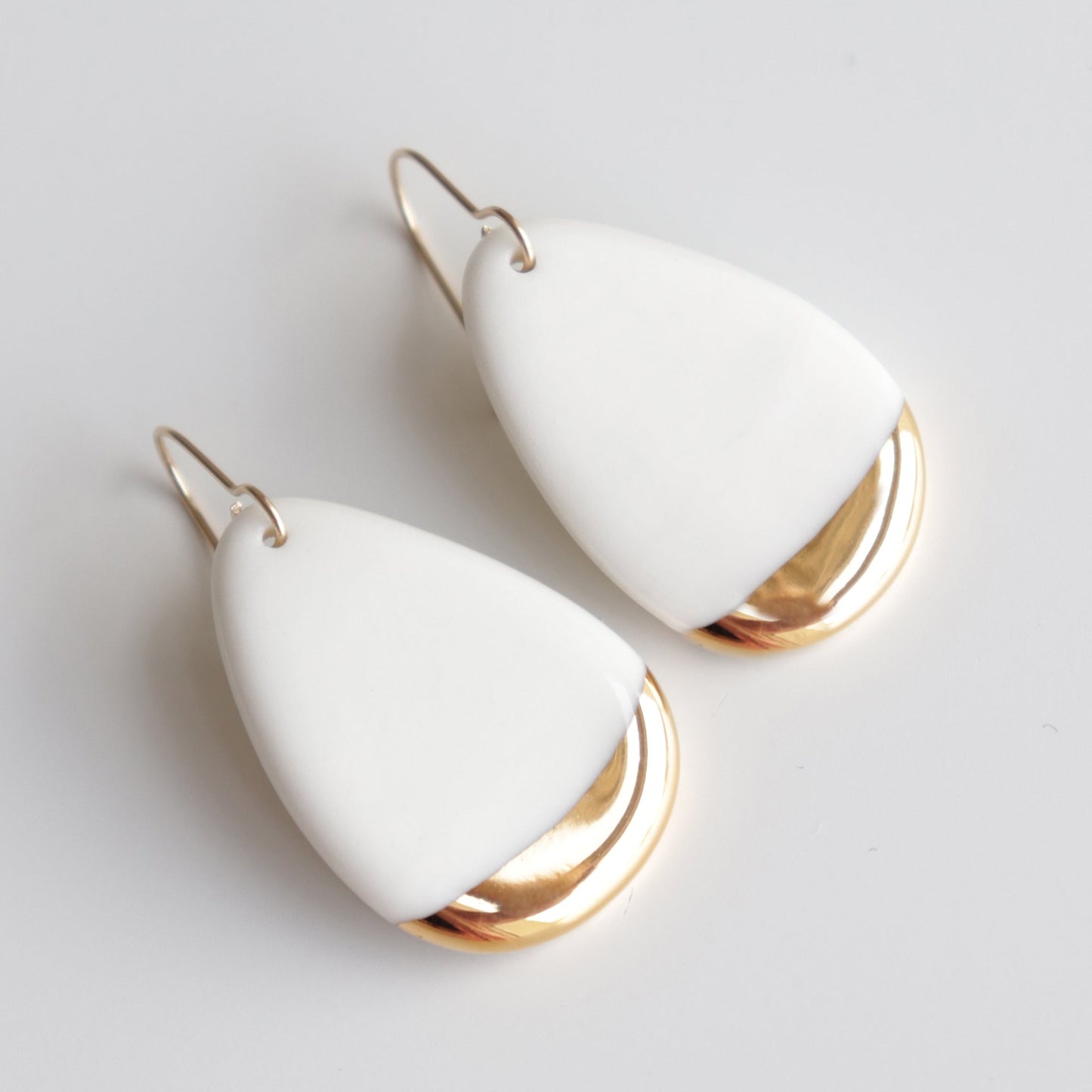 Rozenthal Jewelry’s Drop Earrings / M are handmade porcelain statement earrings from Latvia, featuring a white teardrop shape with a metallic gold accent at the bottom, displayed on a plain white background.