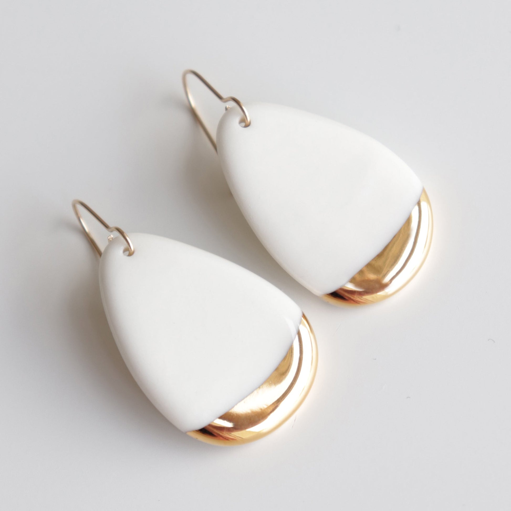 Rozenthal Jewelry’s Drop Earrings / M are handmade porcelain statement earrings from Latvia, featuring a white teardrop shape with a metallic gold accent at the bottom, displayed on a plain white background.
