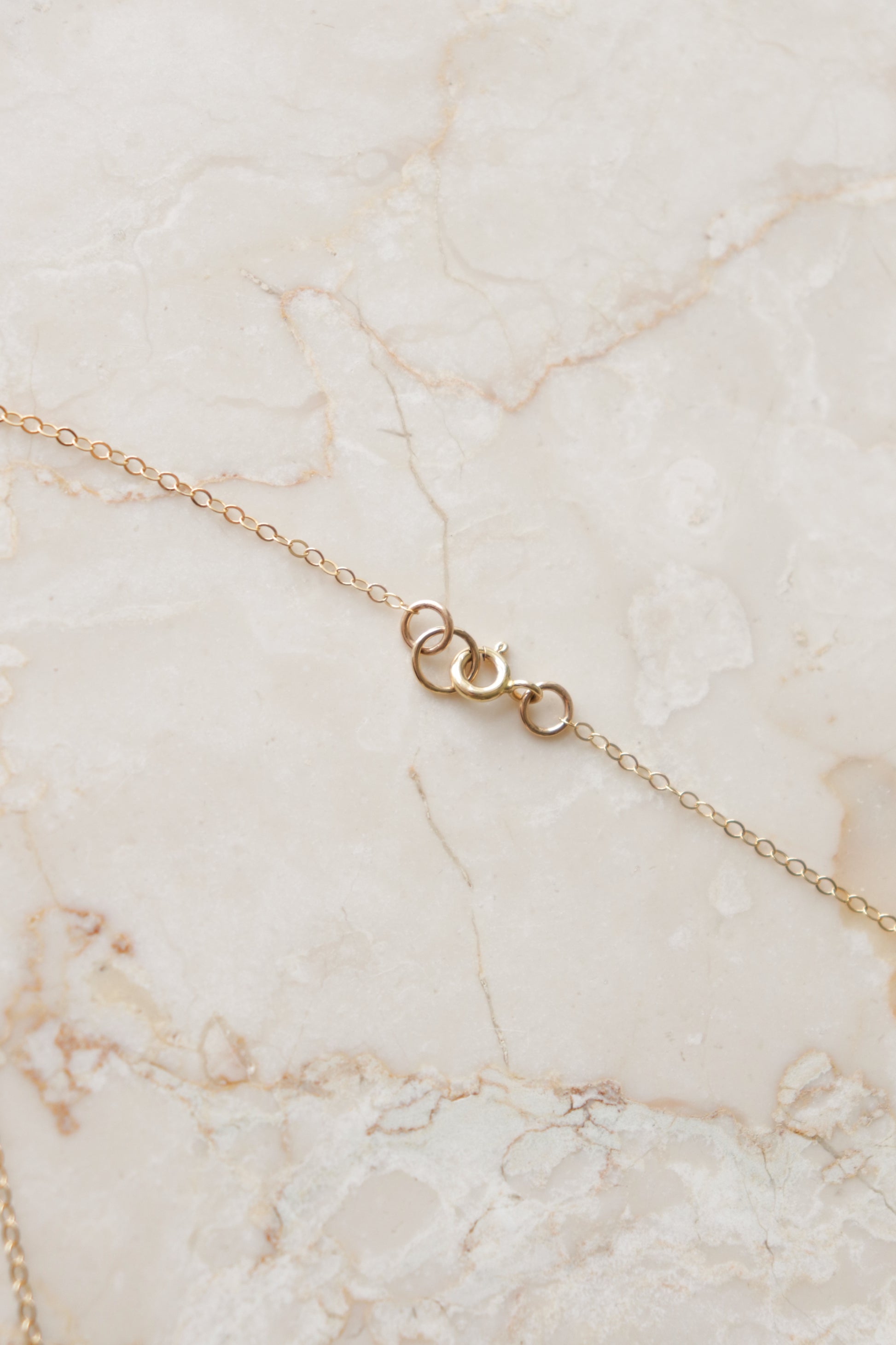 The Leaf Necklace by Rozenthal Jewelry is a delicate gold chain with a small spring ring clasp, ideal for minimalist style lovers, displayed on a light marbled surface.