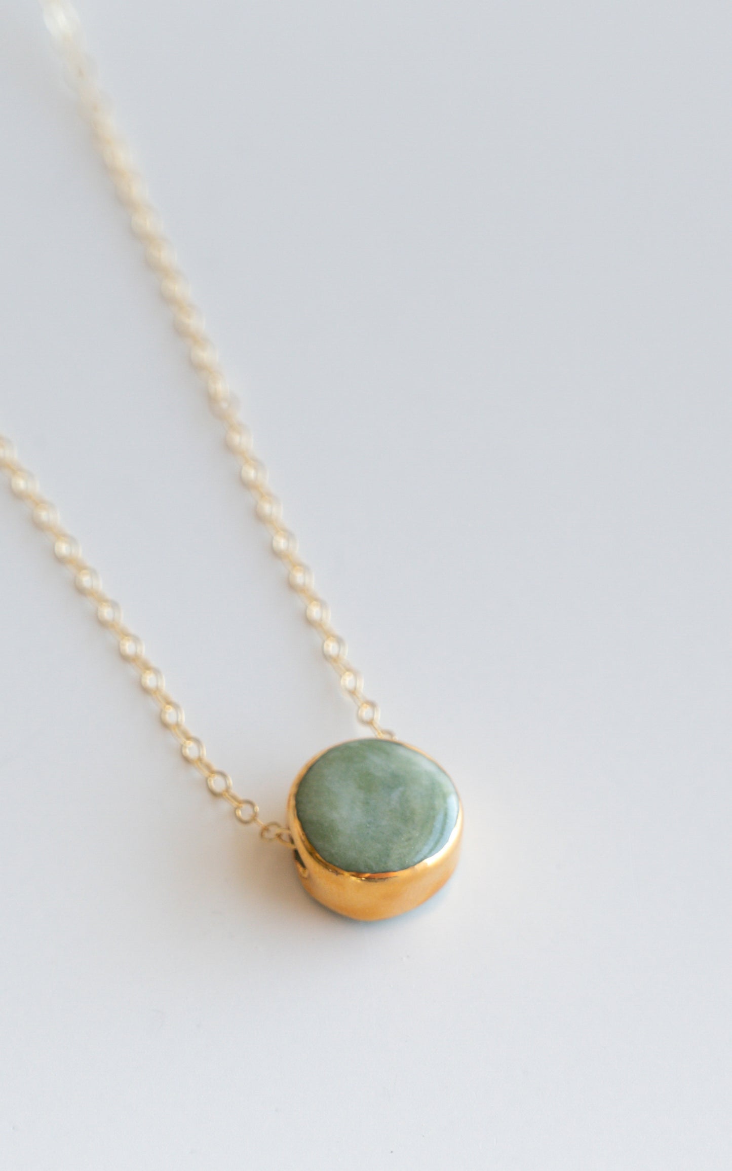 The Round Necklace by Rozenthal Jewelry is a handmade gold chain featuring a round green stone pendant in a gold setting, displayed on a light gray background.