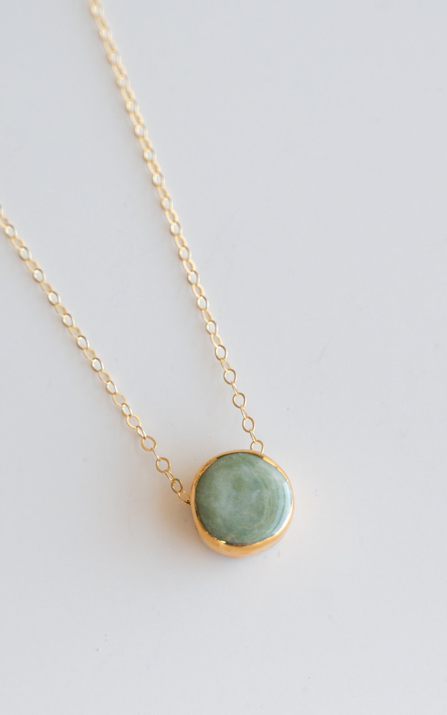 The Rozenthal Jewelry Round Necklace features a minimalist gold chain with a round green stone pendant in a gold bezel setting, shown on a plain white background.
