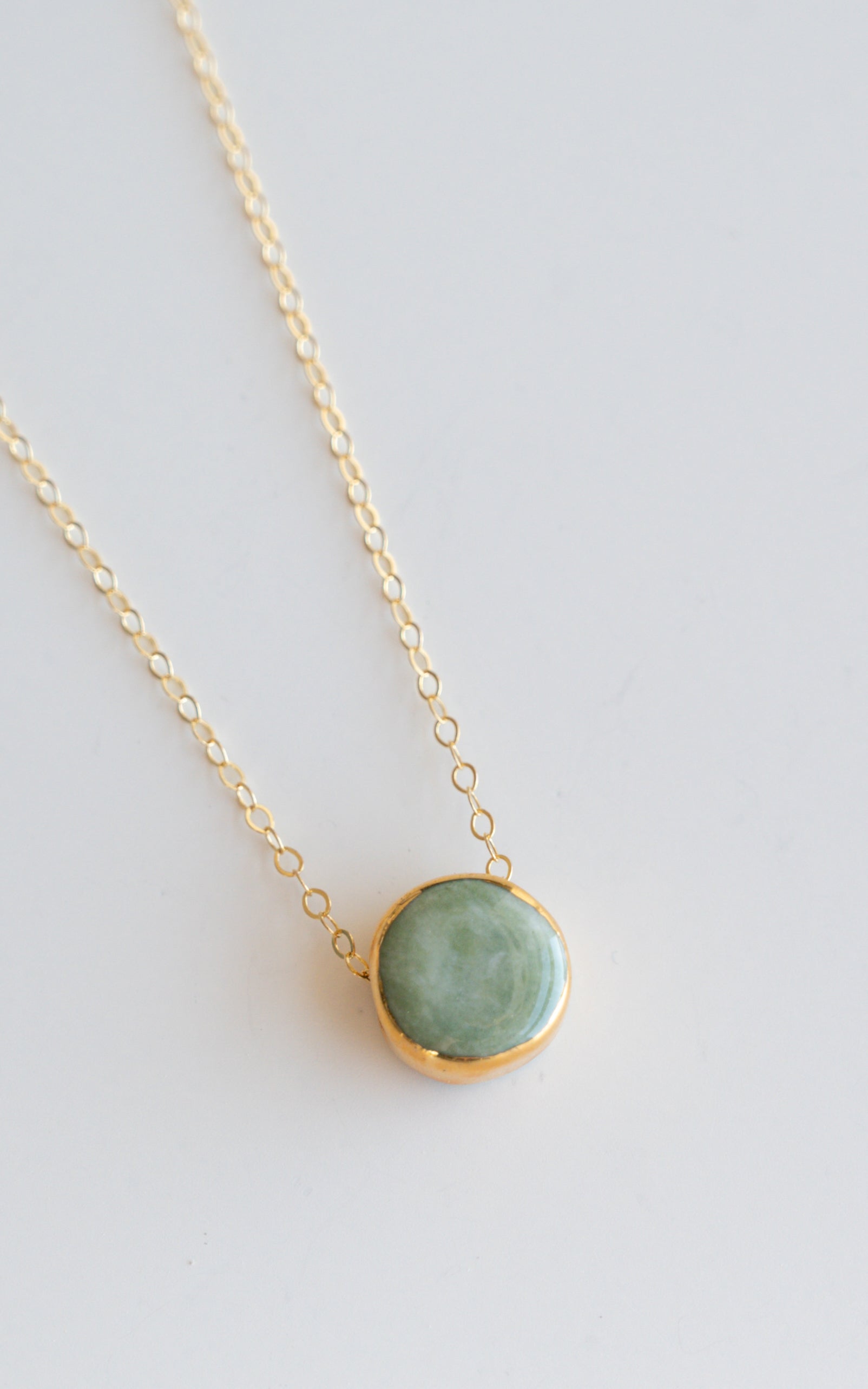 The Rozenthal Jewelry Round Necklace features a minimalist gold chain with a round green stone pendant in a gold bezel setting, shown on a plain white background.