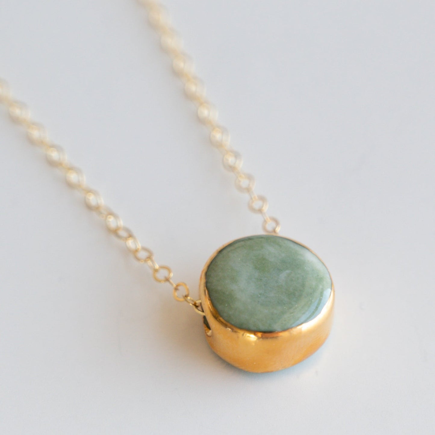 The Round Necklace by Rozenthal Jewelry features a gold chain with a round jade green stone in a gold bezel pendant, showcased against a plain light background.