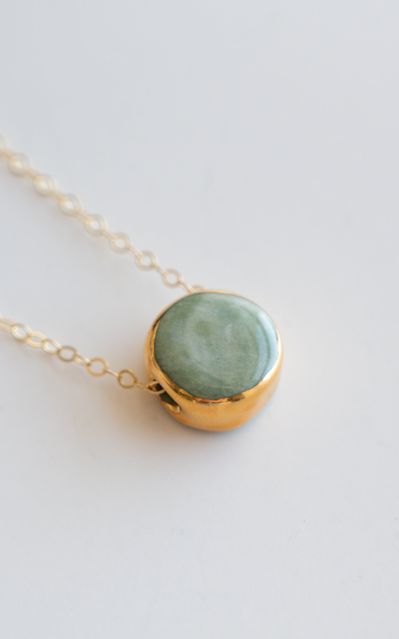 A close-up of the Round Necklace by Rozenthal Jewelry features a gold chain with a round green stone pendant set in a gold frame on a light background—ideal for fans of minimalist jewelry and timeless elegance.