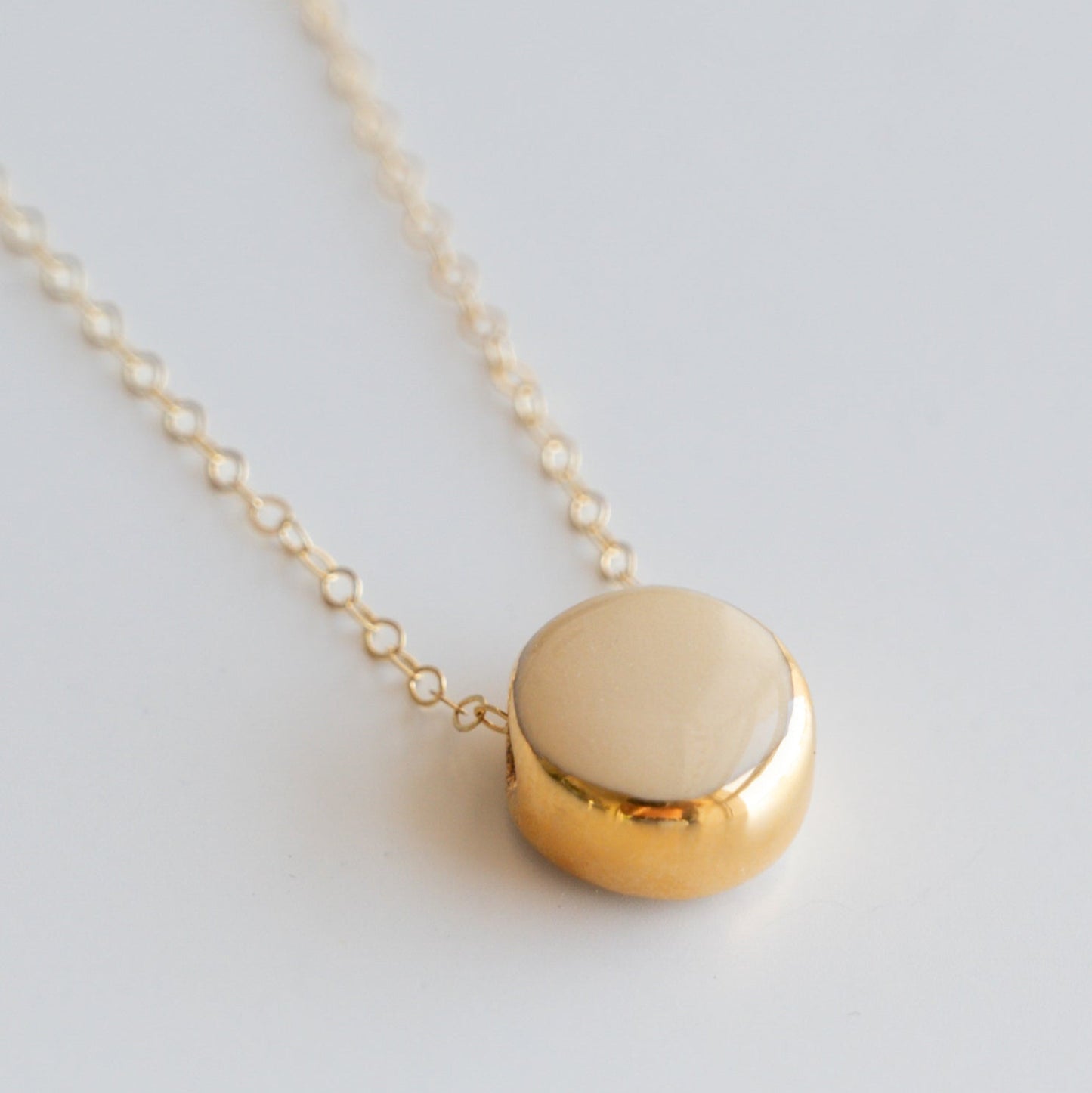 The Round Necklace by Rozenthal Jewelry is a minimalist gold chain with a smooth round pendant and creamy beige porcelain center, shown on a white background.