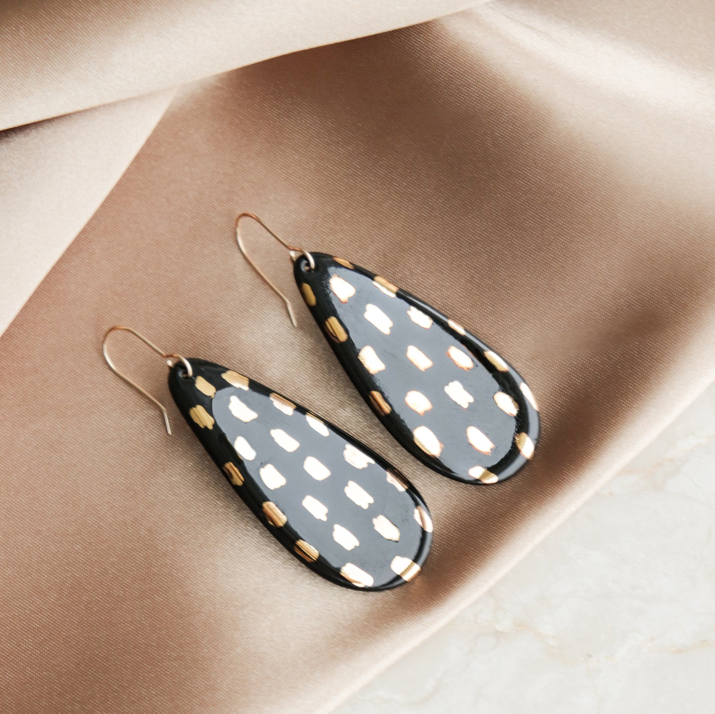 Drop Earrings / L by Rozenthal Jewelry—teardrop porcelain earrings with black and gold spots, shown on beige satin. Ideal for fans of minimalist jewelry.