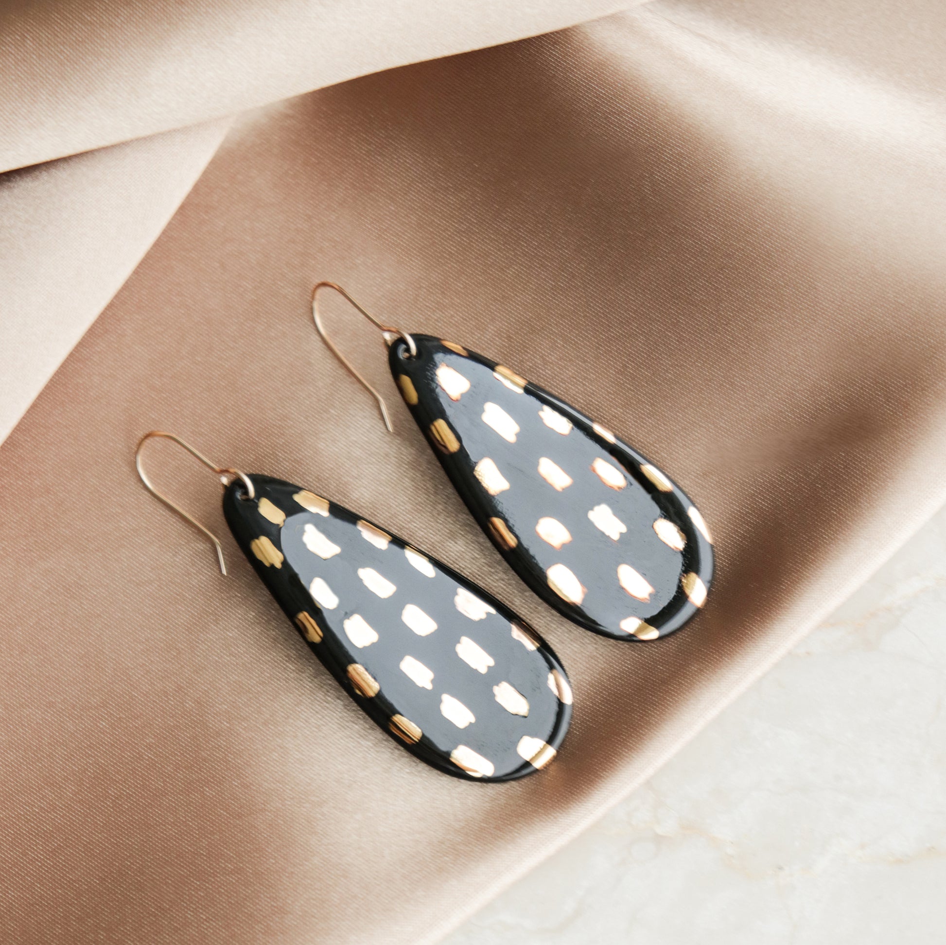 Drop Earrings / L by Rozenthal Jewelry—teardrop porcelain earrings with black and gold spots, shown on beige satin. Ideal for fans of minimalist jewelry.