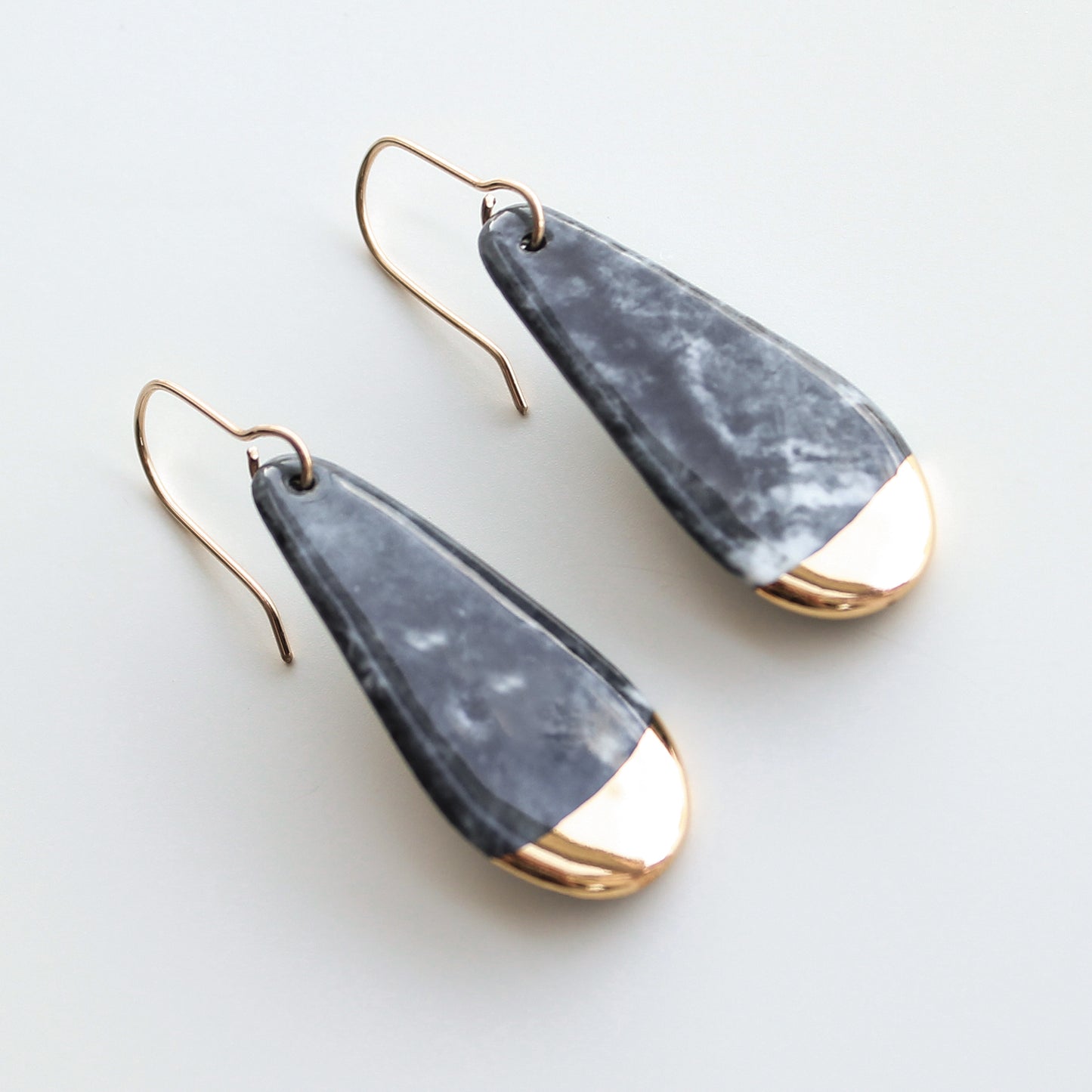 Drop earrings / S by Rozenthal Jewelry: teardrop-shaped, handmade in Latvia with marbled gray bodies and shiny gold tips on thin gold hooks, shown against a light background.
