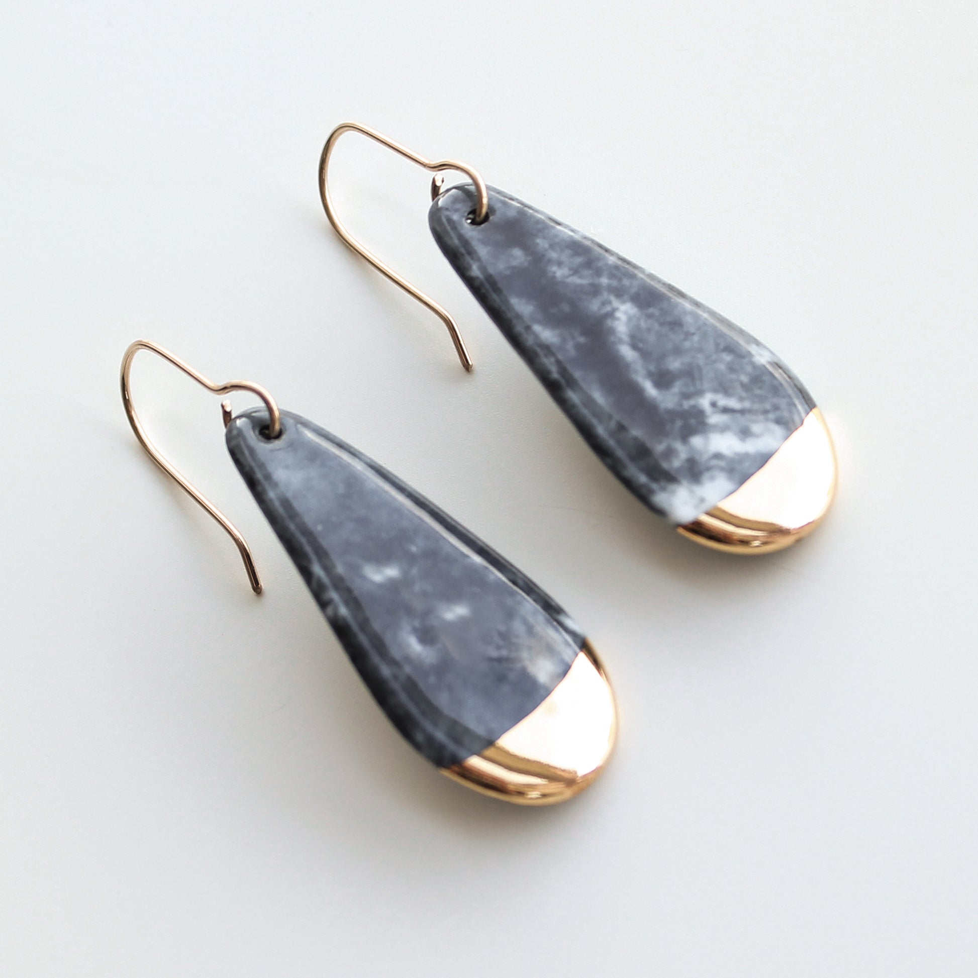 Drop earrings / S by Rozenthal Jewelry: teardrop-shaped, handmade in Latvia with marbled gray bodies and shiny gold tips on thin gold hooks, shown against a light background.